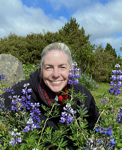 A woman smiling in front of a bunch of flowers.