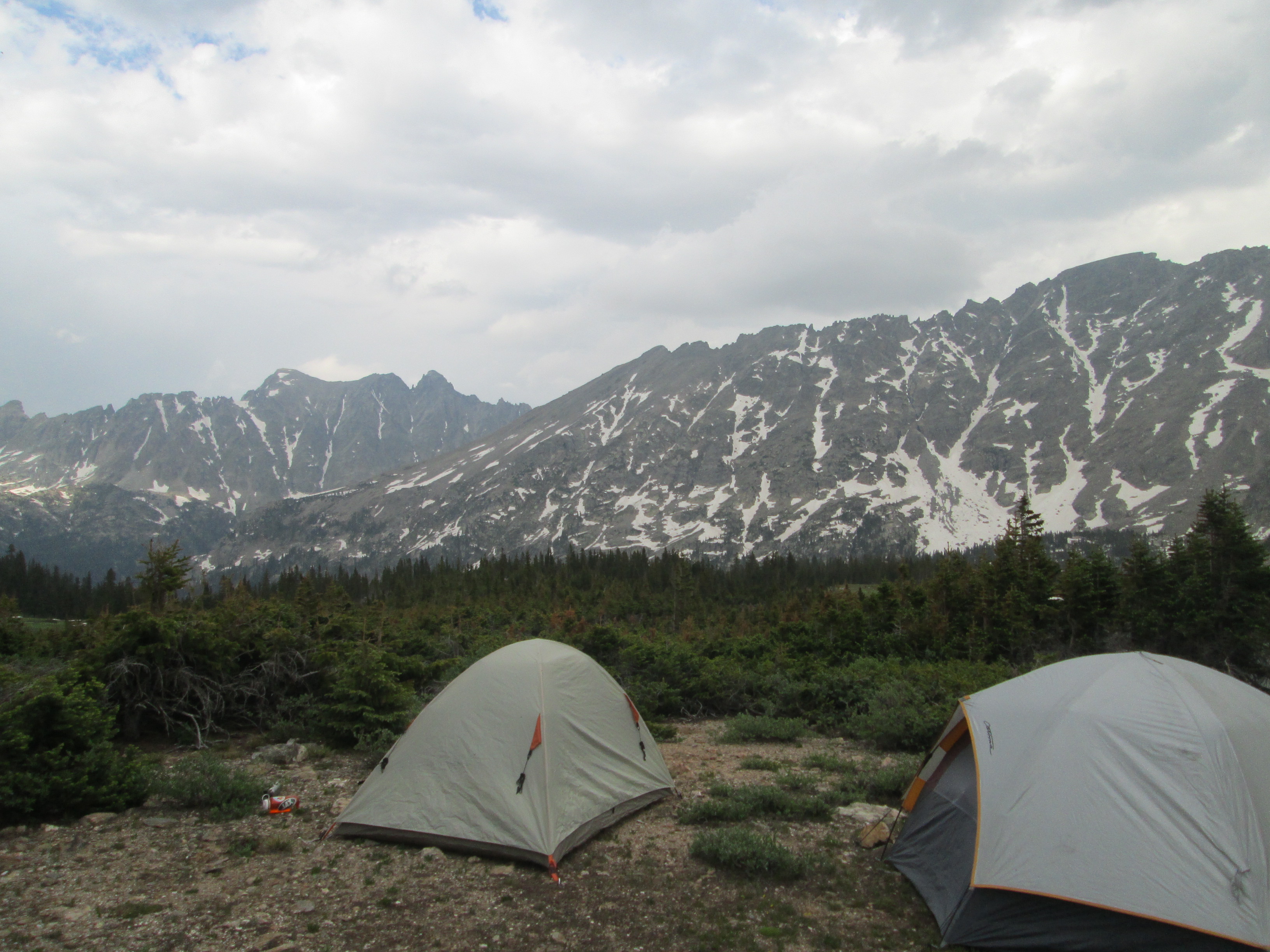 Two tents situated on a mountain around a green field