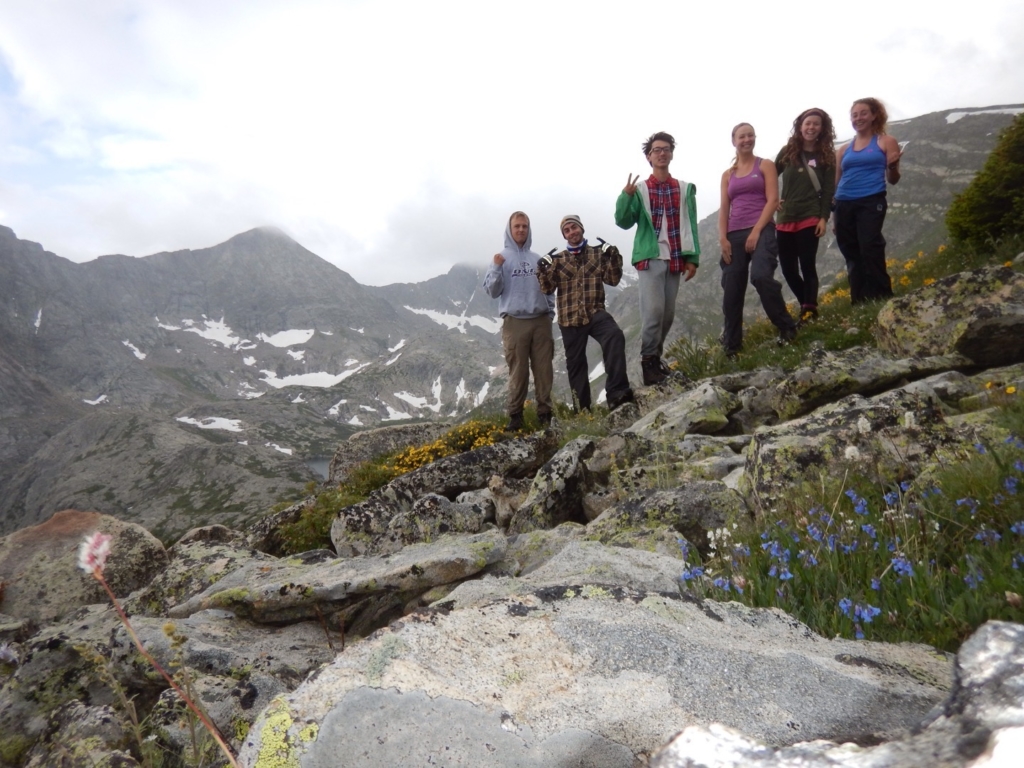 A group of five hikers smiling on a rocky mountain slope