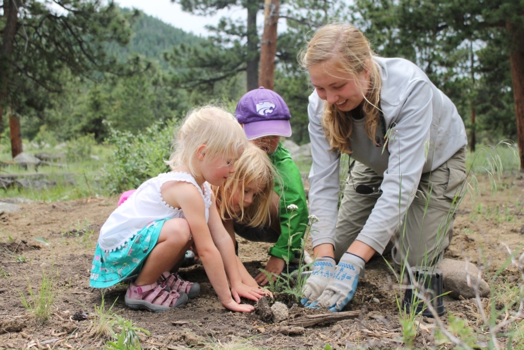 A woman and three young children plant saplings in a forest clearing