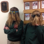 Two people wearing green sweatshirts and sunglasses, with their long hair covering their faces