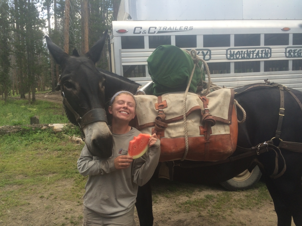 Woman smiling with a slice of watermelon next to a packed horse