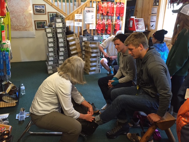 Woman fitting a boot to a man with people waiting in line on the background