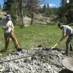 Two men are digging a hole in the ground with shovels.