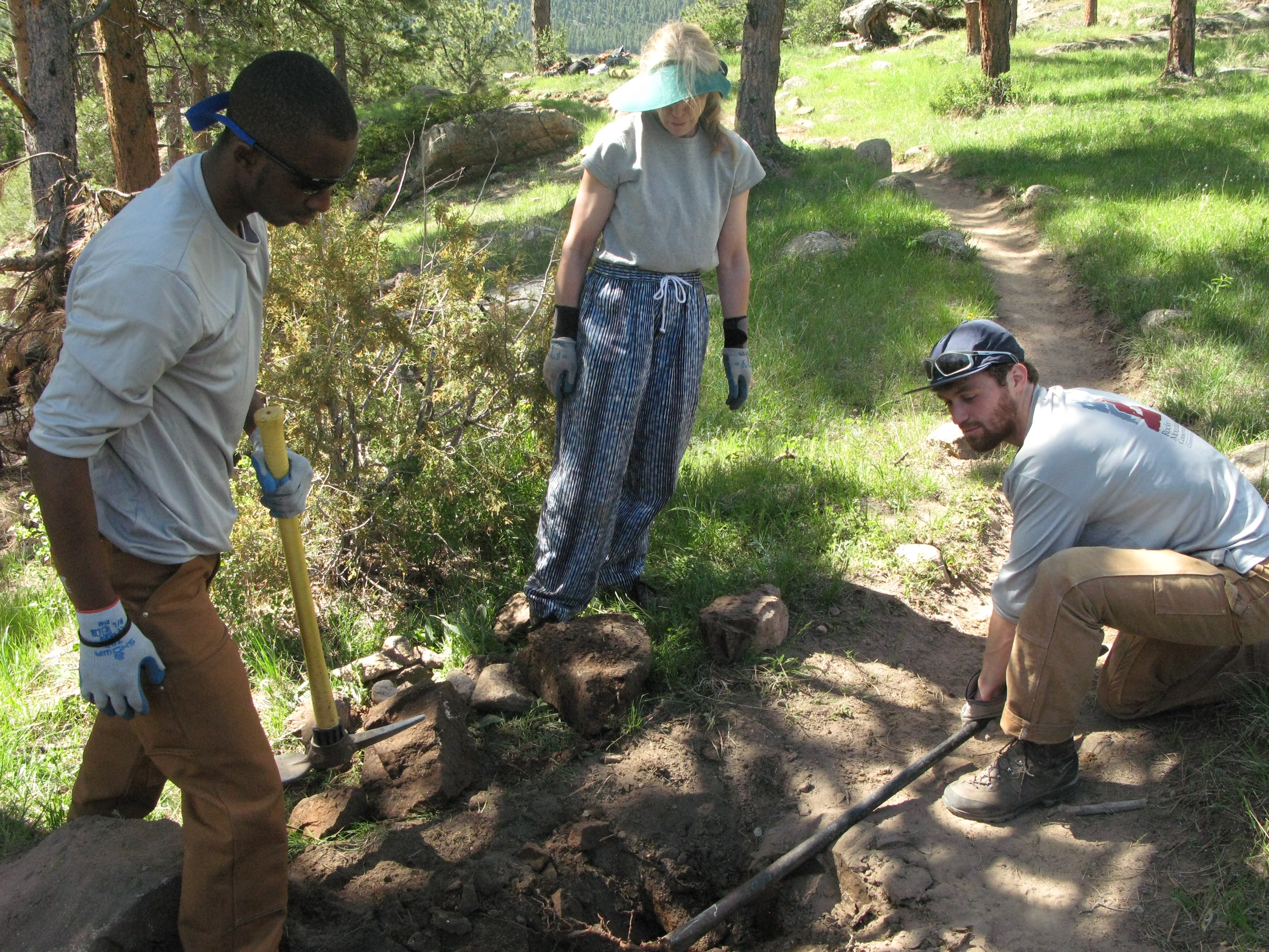 Three people digging on a forest to create a trail