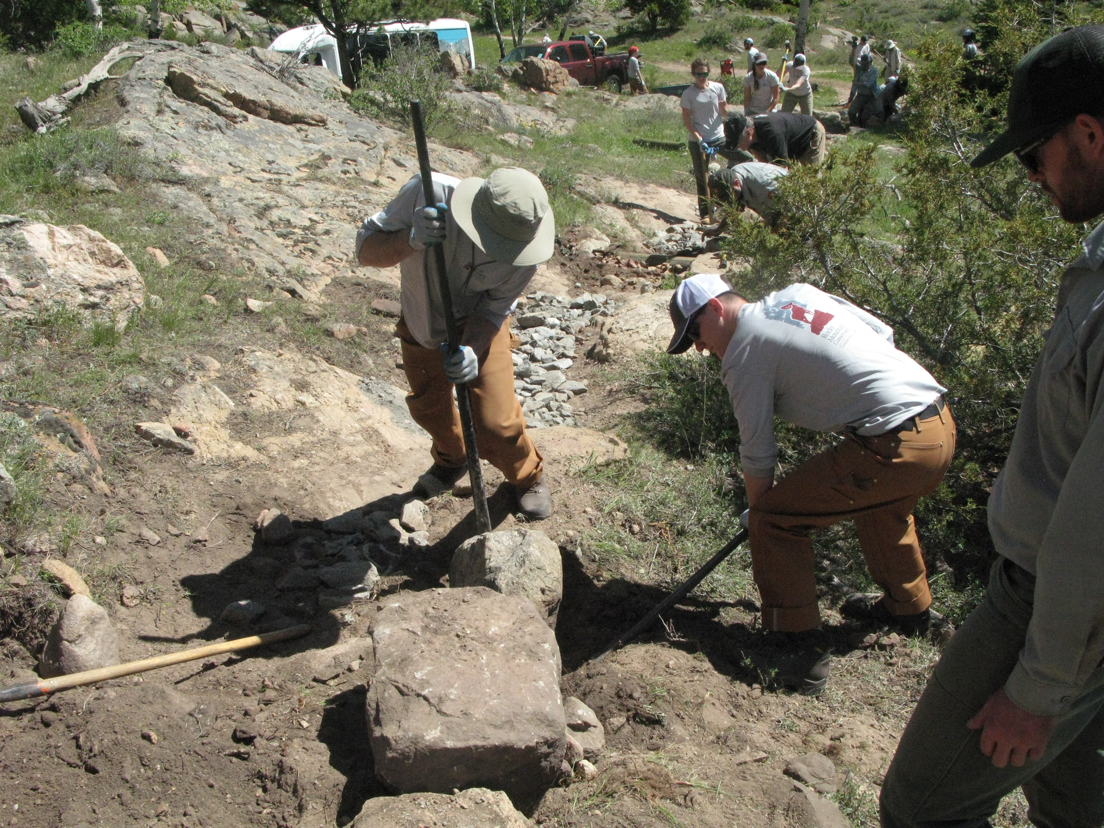 Two worker attempting to lift a large rock to build a trail