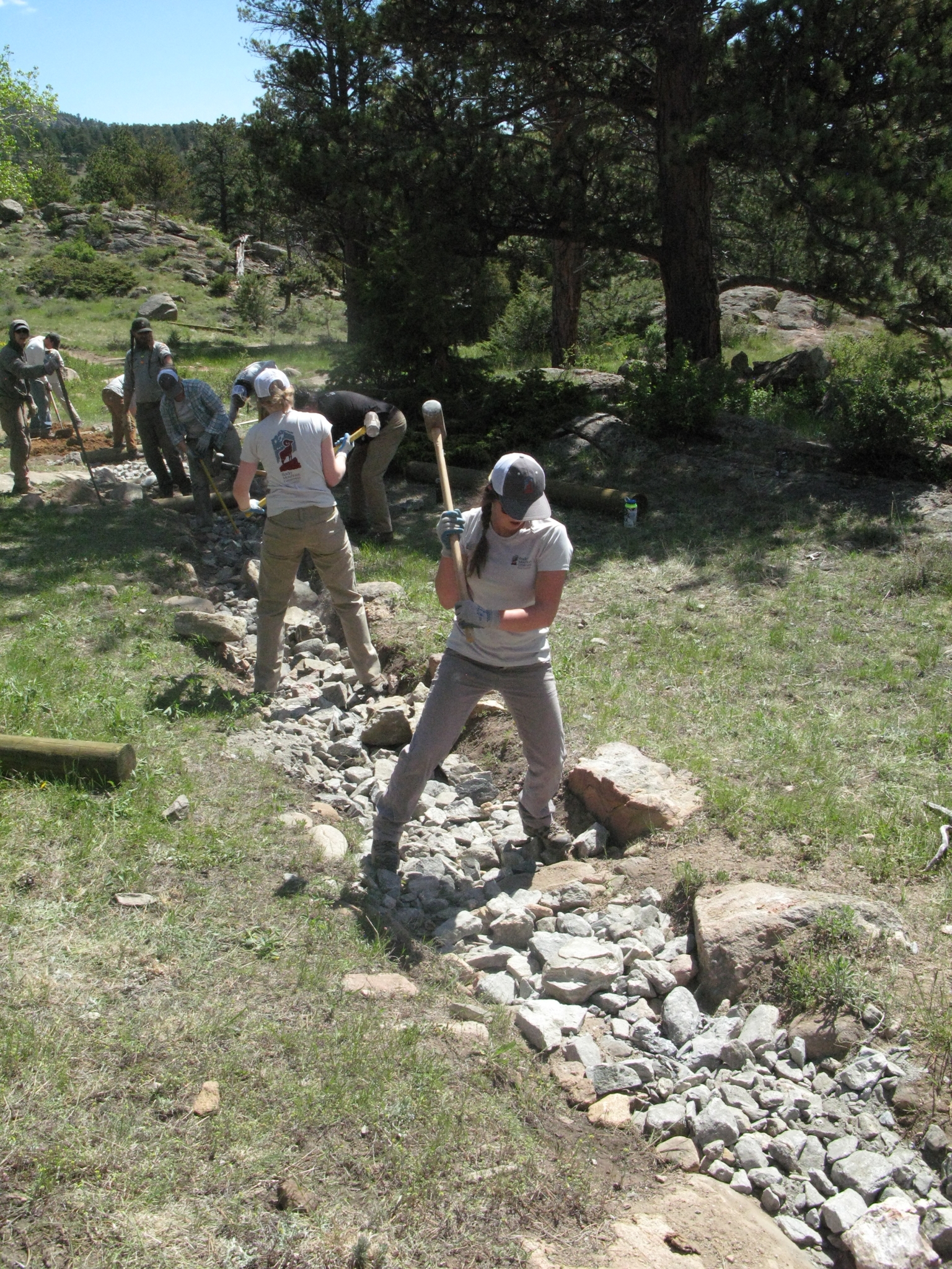 Group of workers smashing small rocks along a trail in a mountainous area