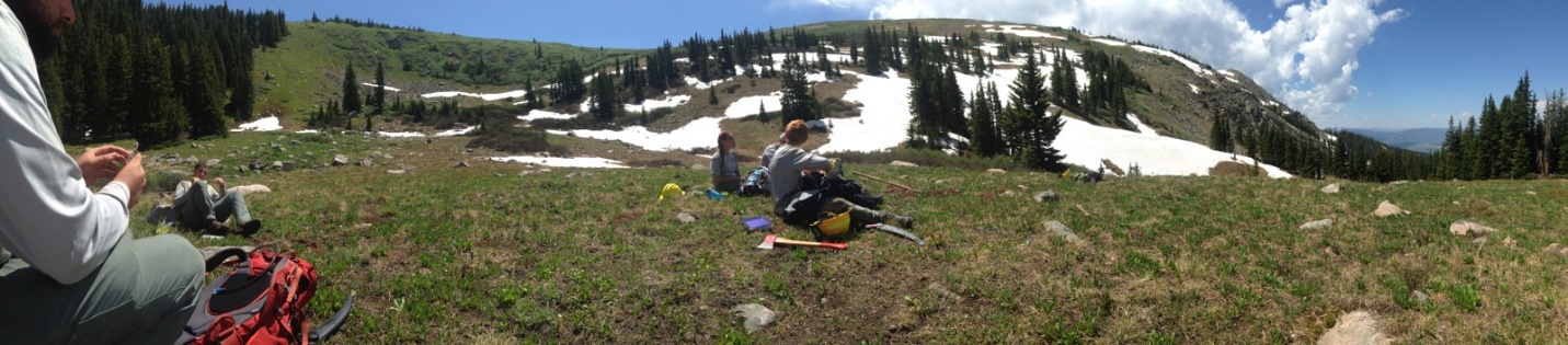 Panoramic view of hikers resting in a mountainous meadow with patches of snow