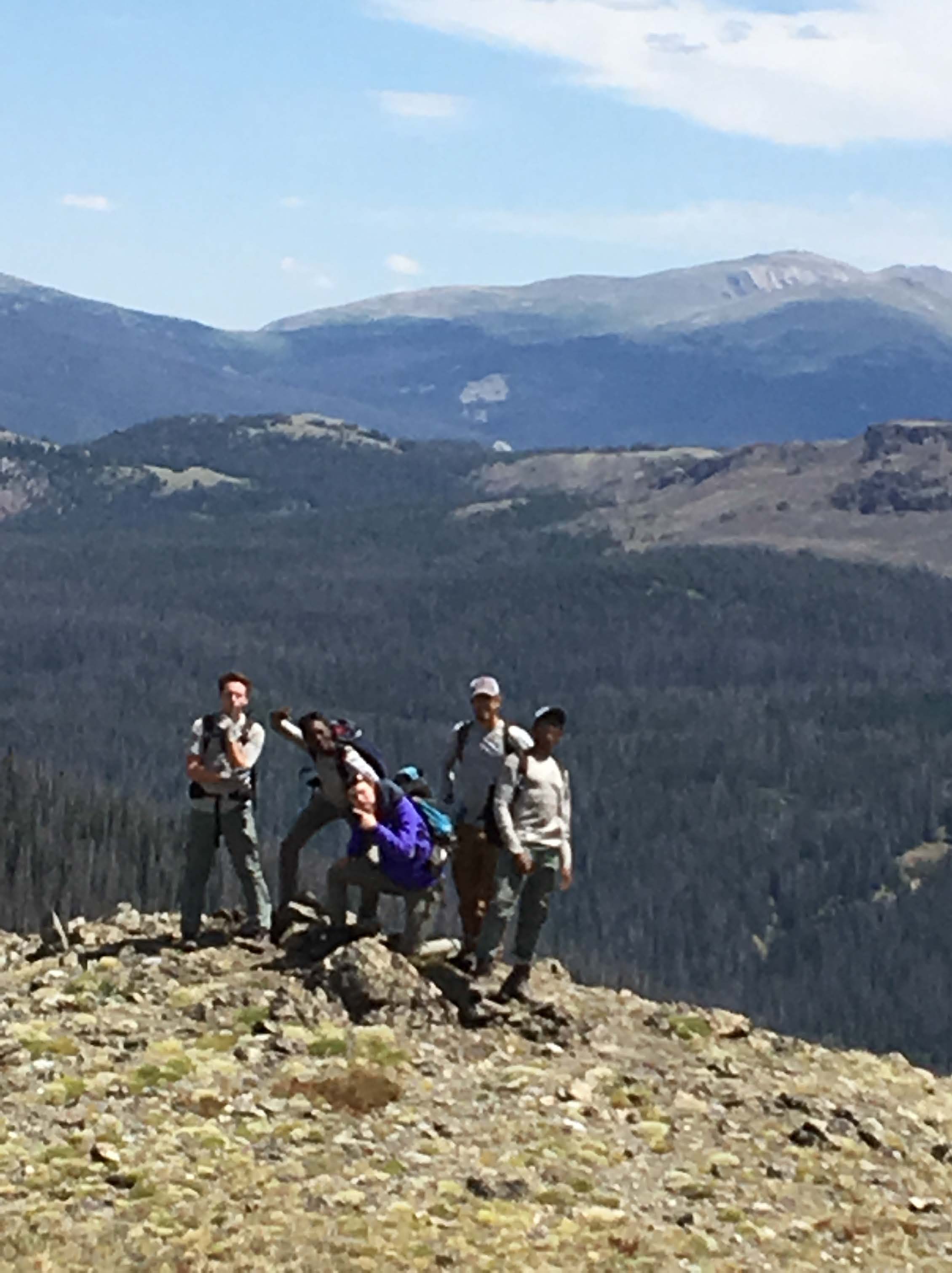 Four hikers posing on a rocky mountaintop with a panoramic view