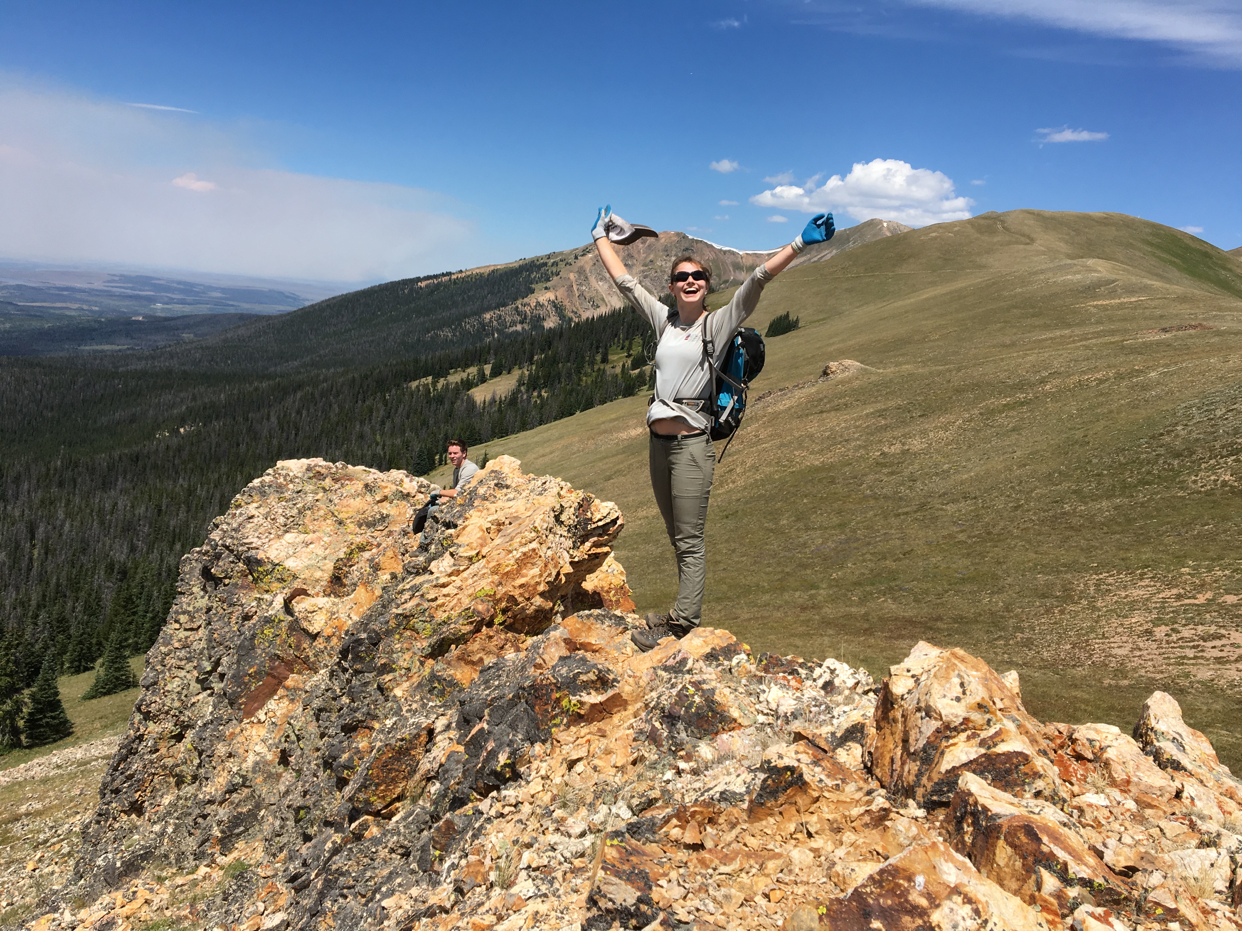 A woman triumphantly raises her arms on a rocky mountain summit