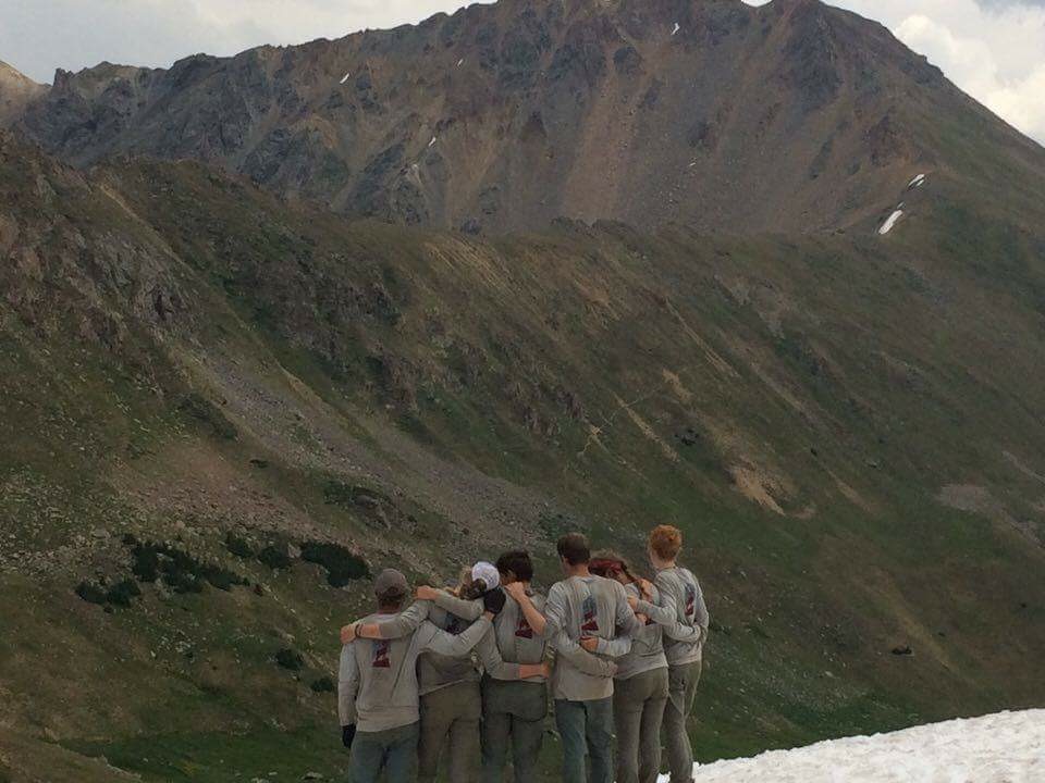 Group of people with arms around each other looking at mountainous terrain