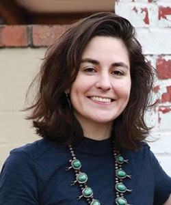 A woman wearing a blue shirt and a necklace.