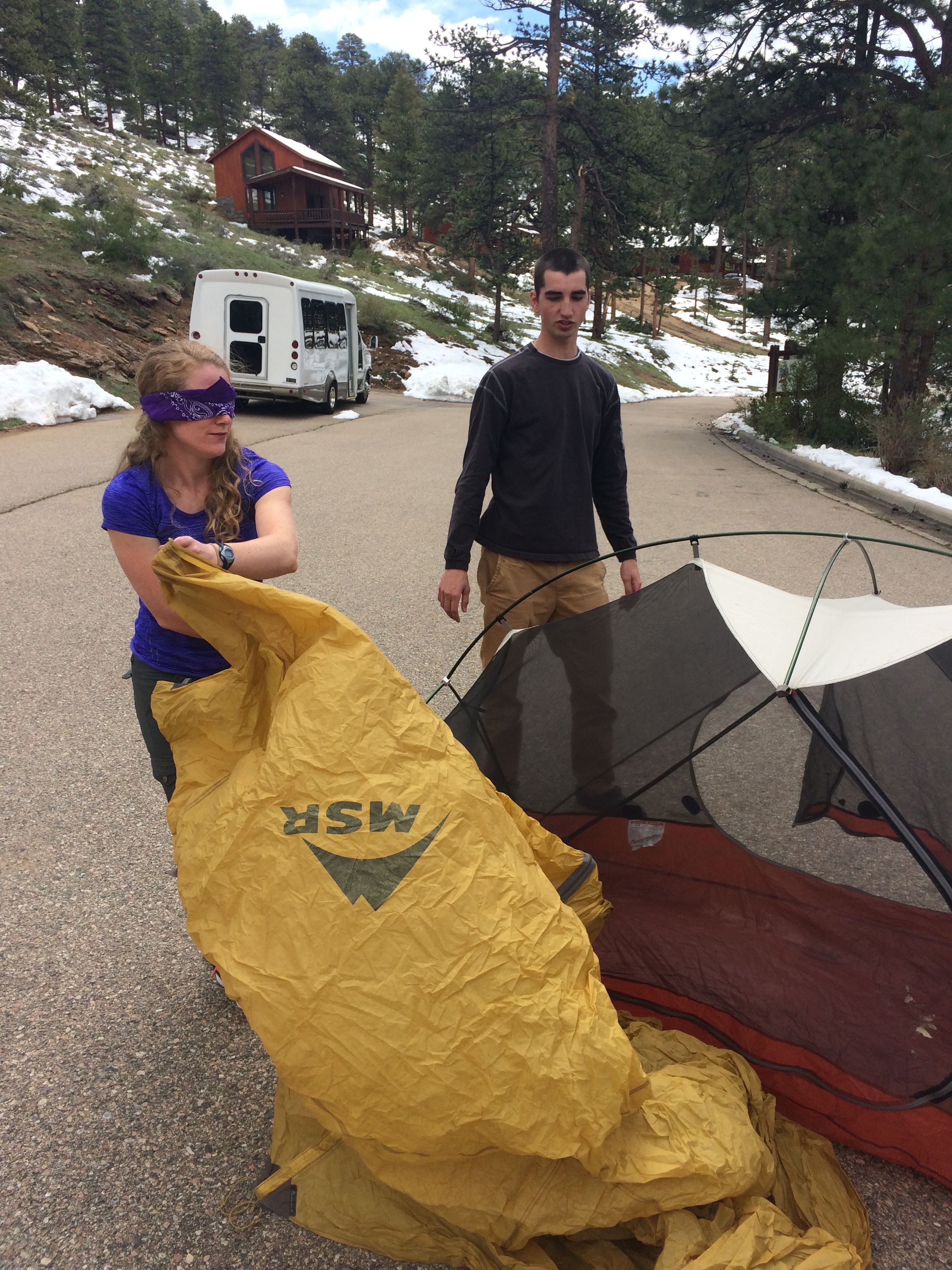 A man and a woman folding a tent on a paved road in a wooded area