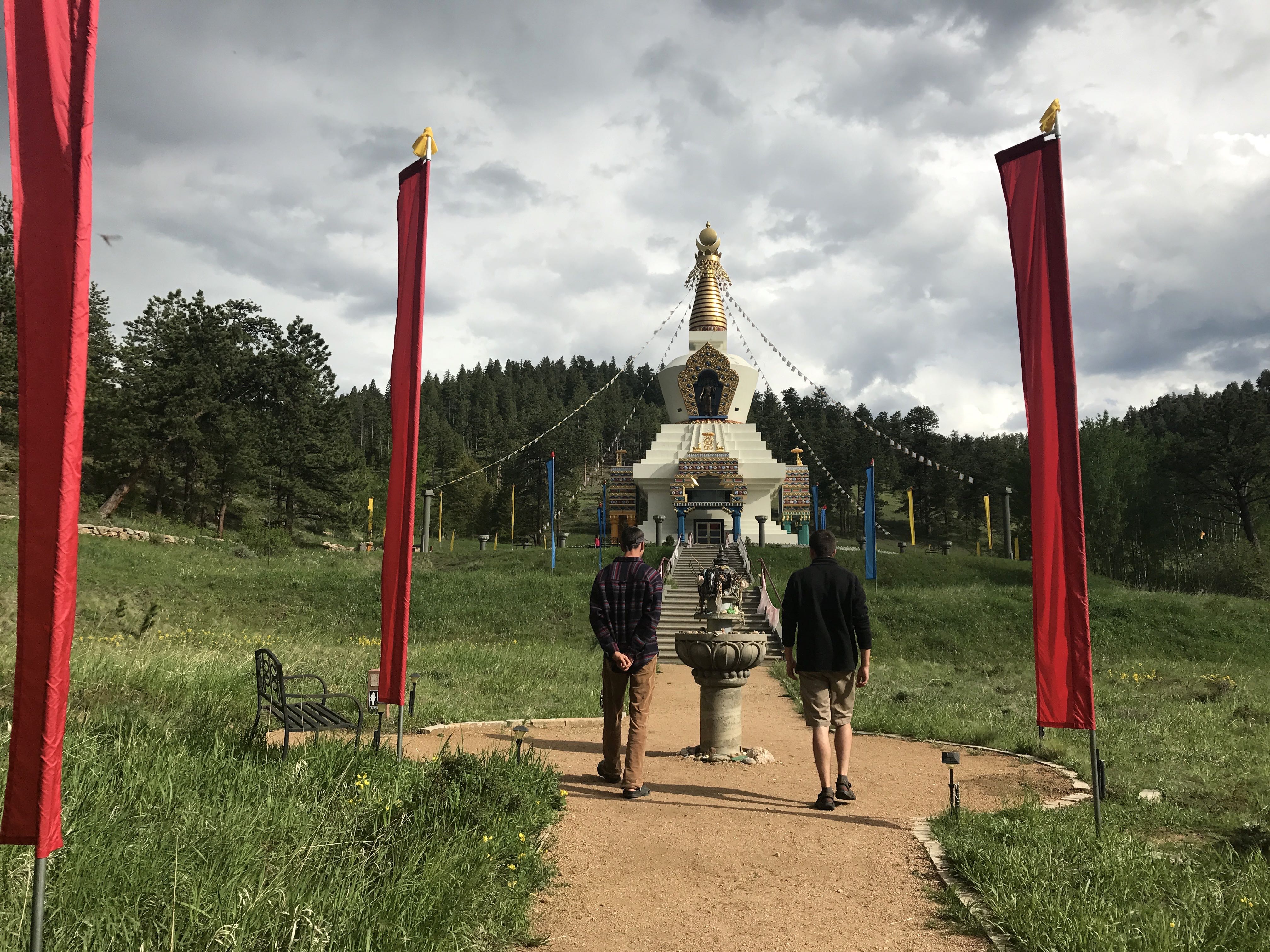 Two people walking towards a white buddhist stupa flanked by red flags