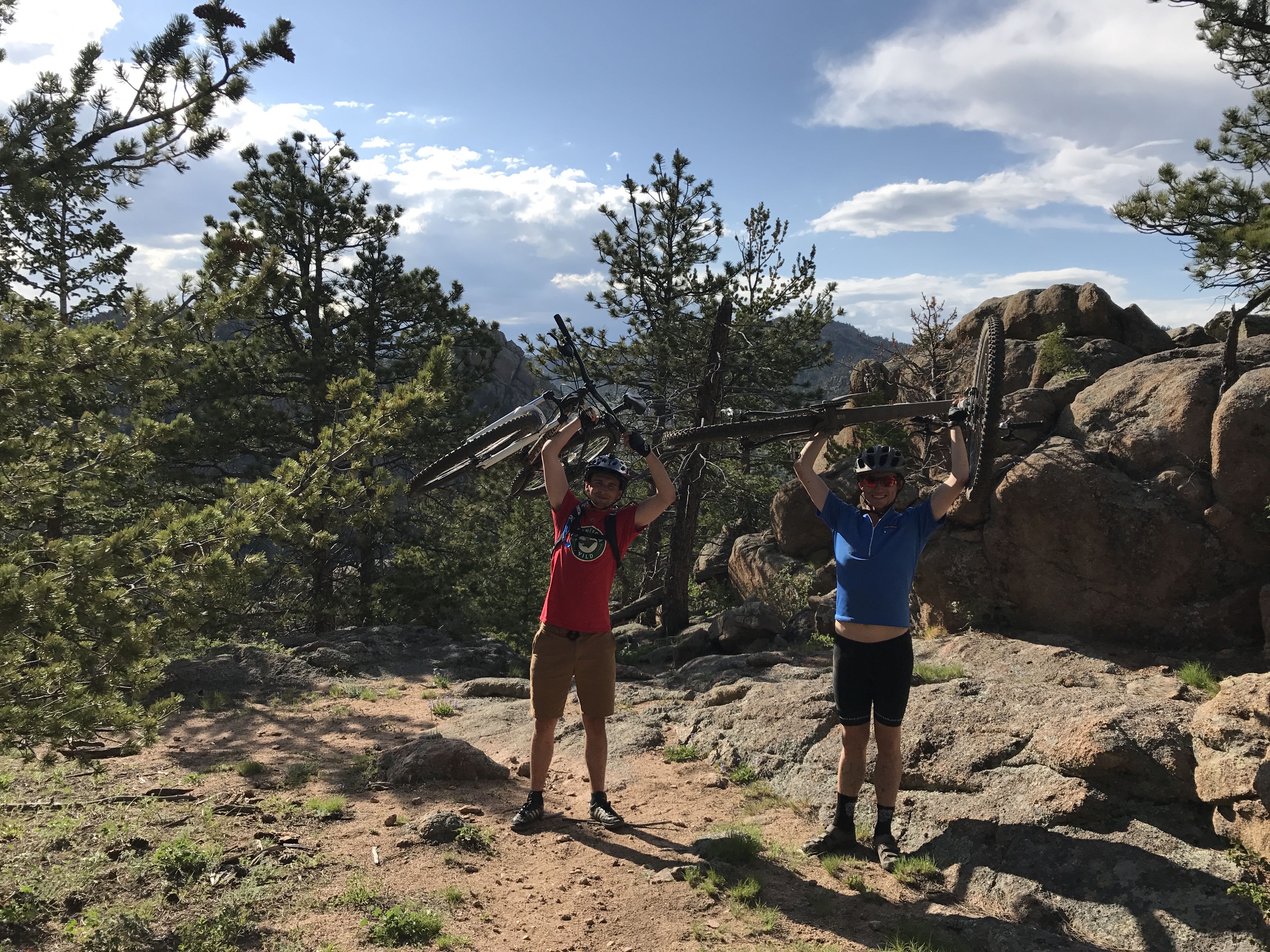 Two men carrying mountain bikes over their heads on a rocky trail