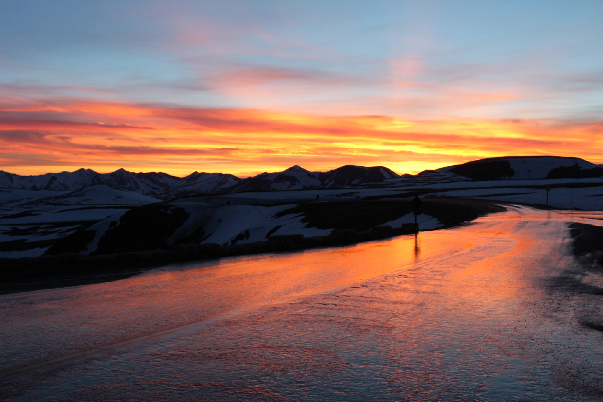 A vibrant sunset over a snowy landscape with a winding road reflecting the vivid orange and red sky.