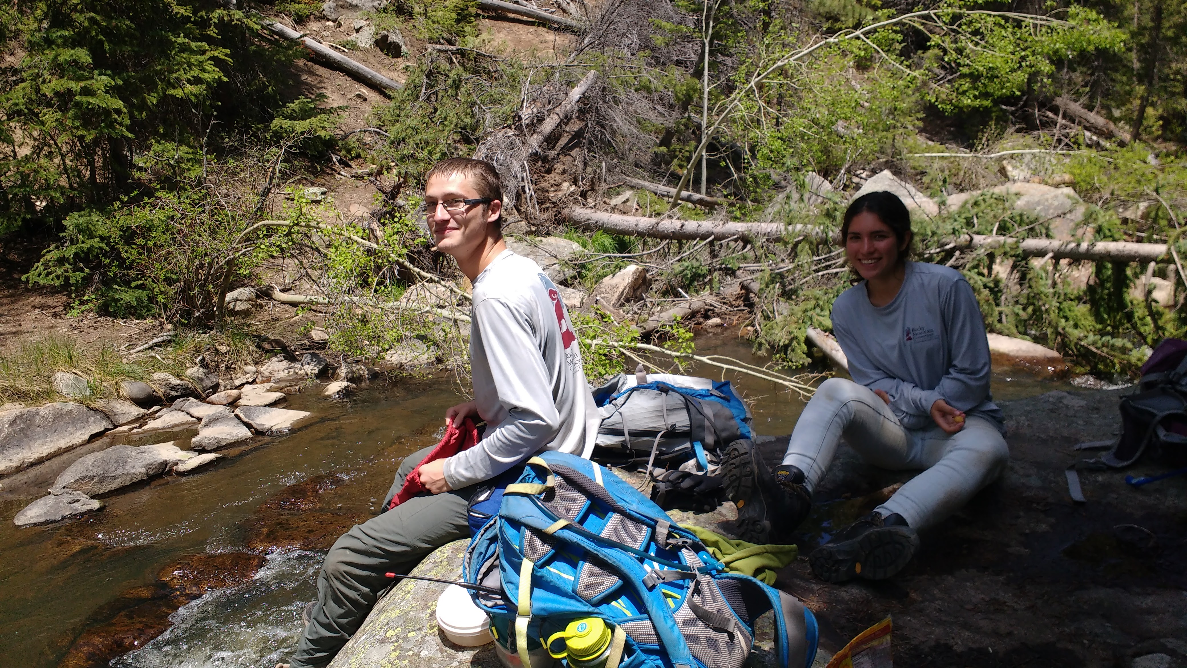 Two people sitting by a stream with backpacks