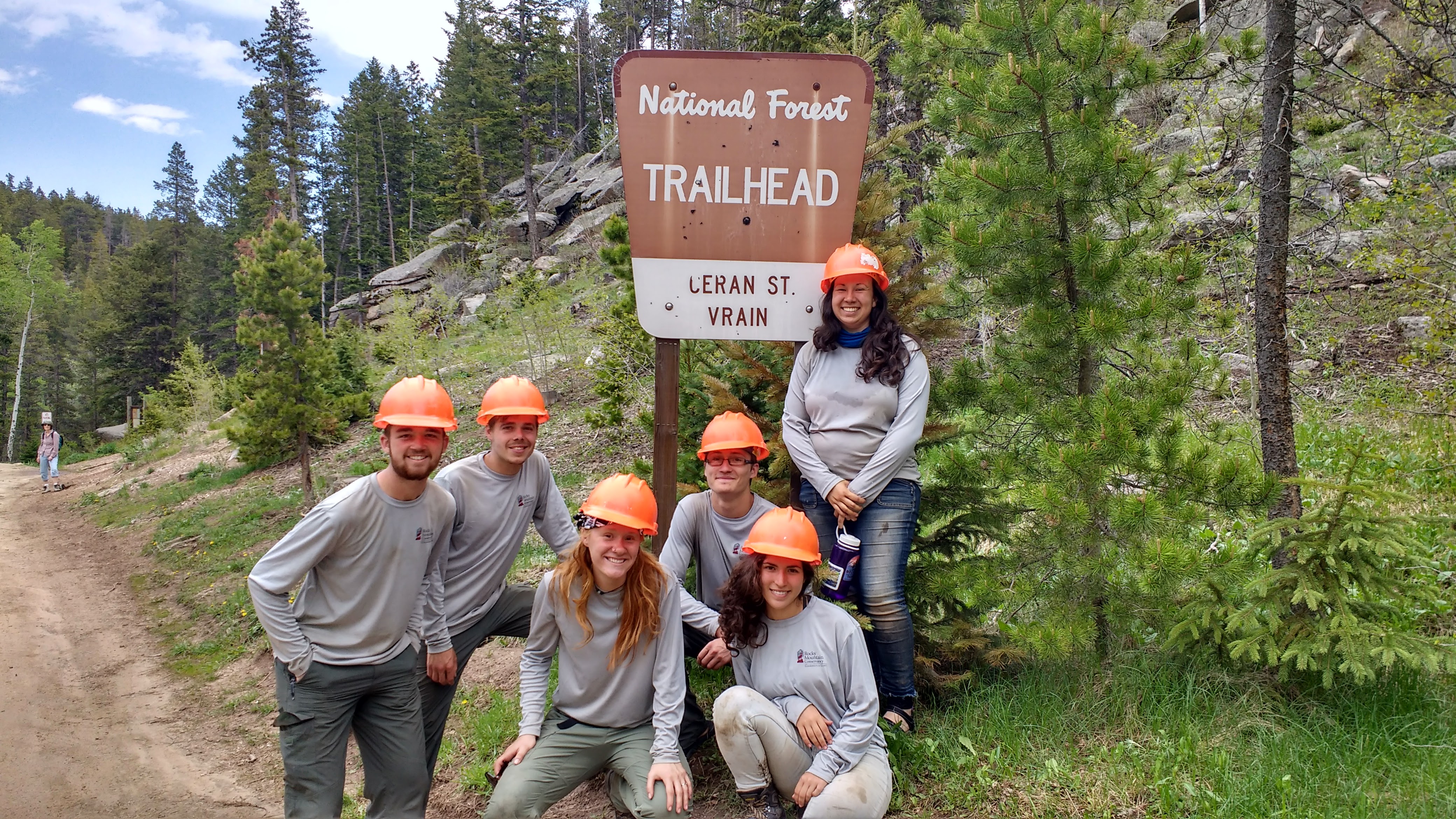 Group of seven people posing by a "national forest trailhead" sign in a wooded area.