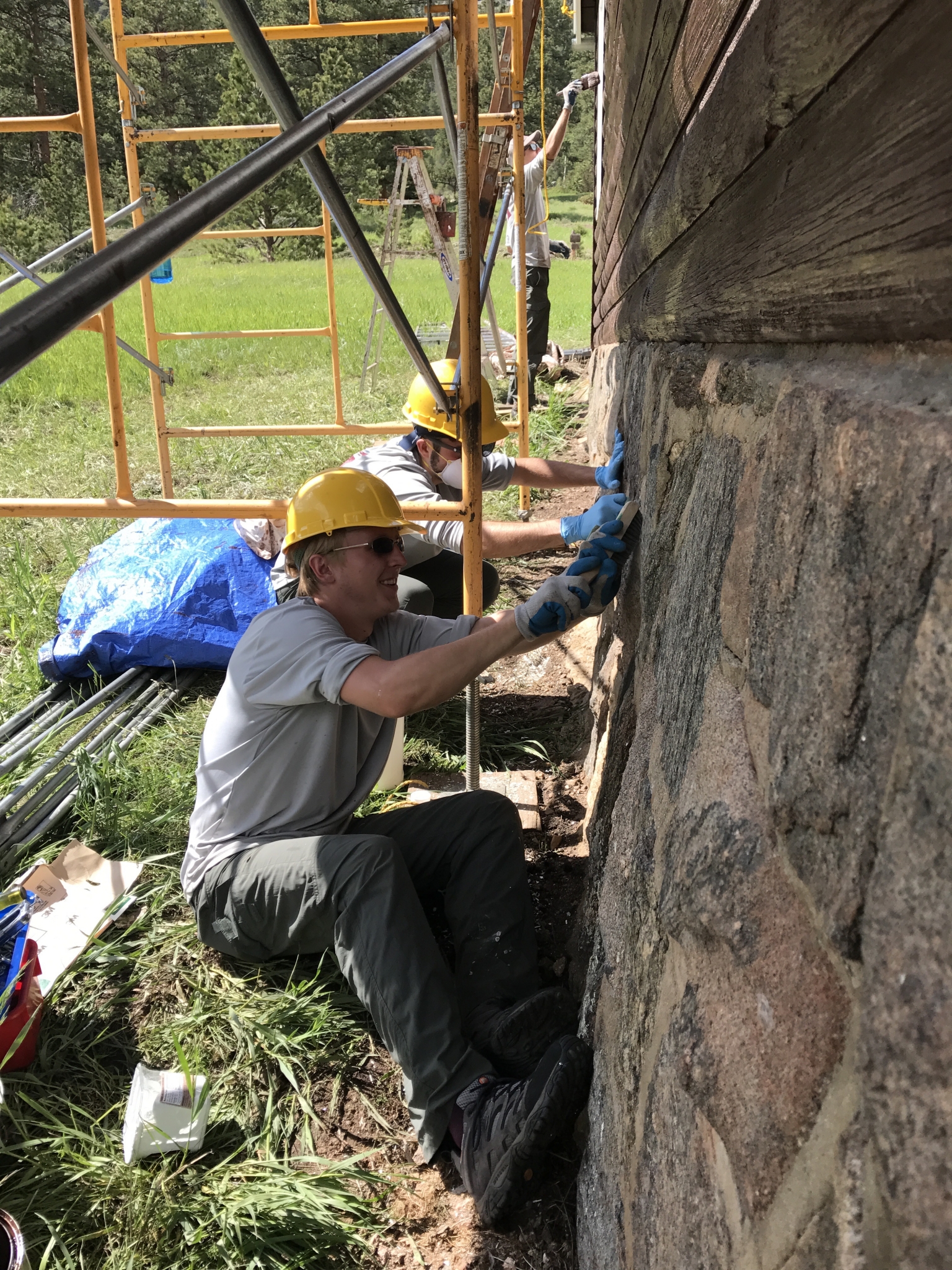 Two construction workers in hard hats and gloves working on a stone wall