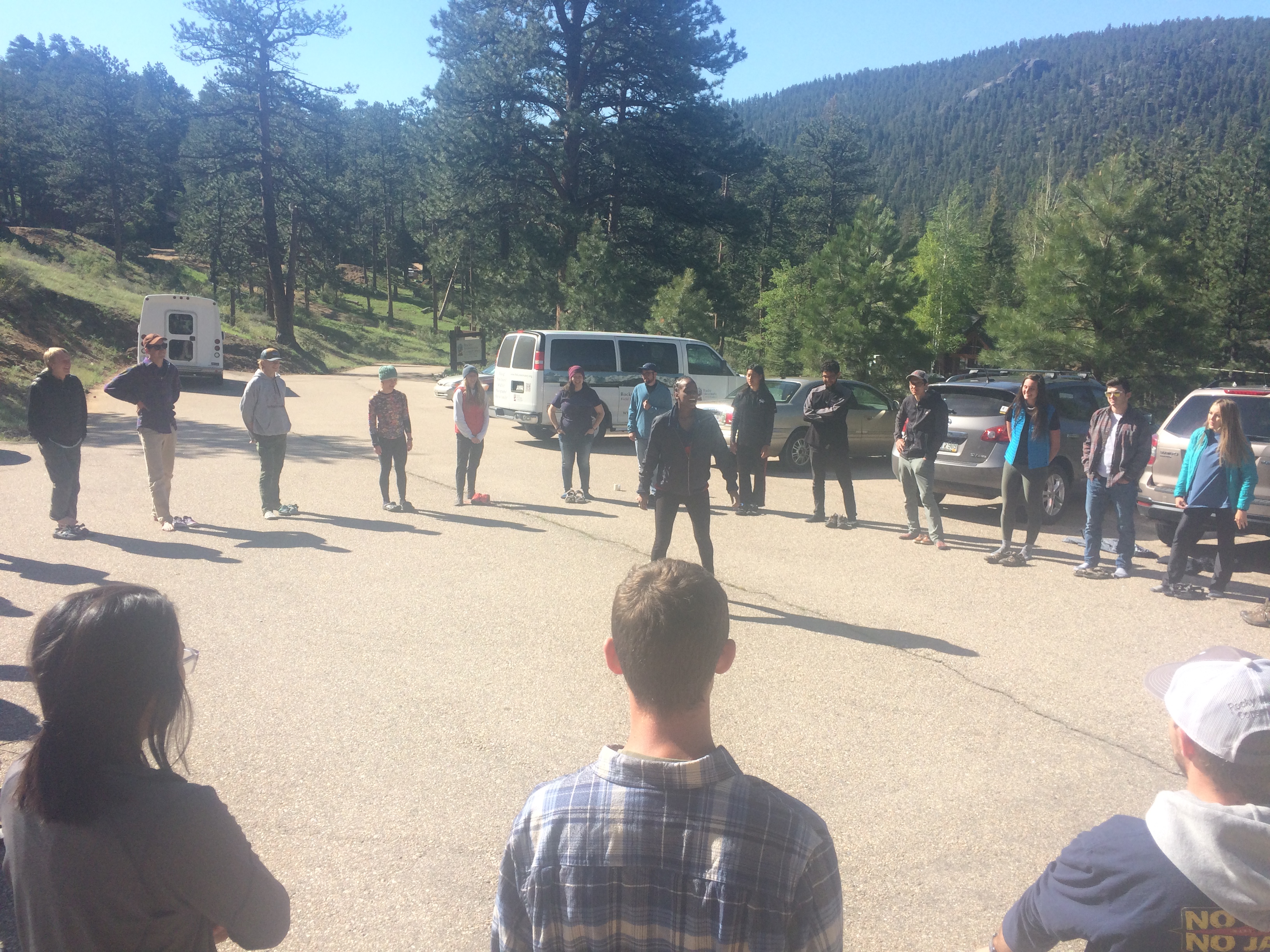 A group of people standing in a circle in a parking area surrounded by trees