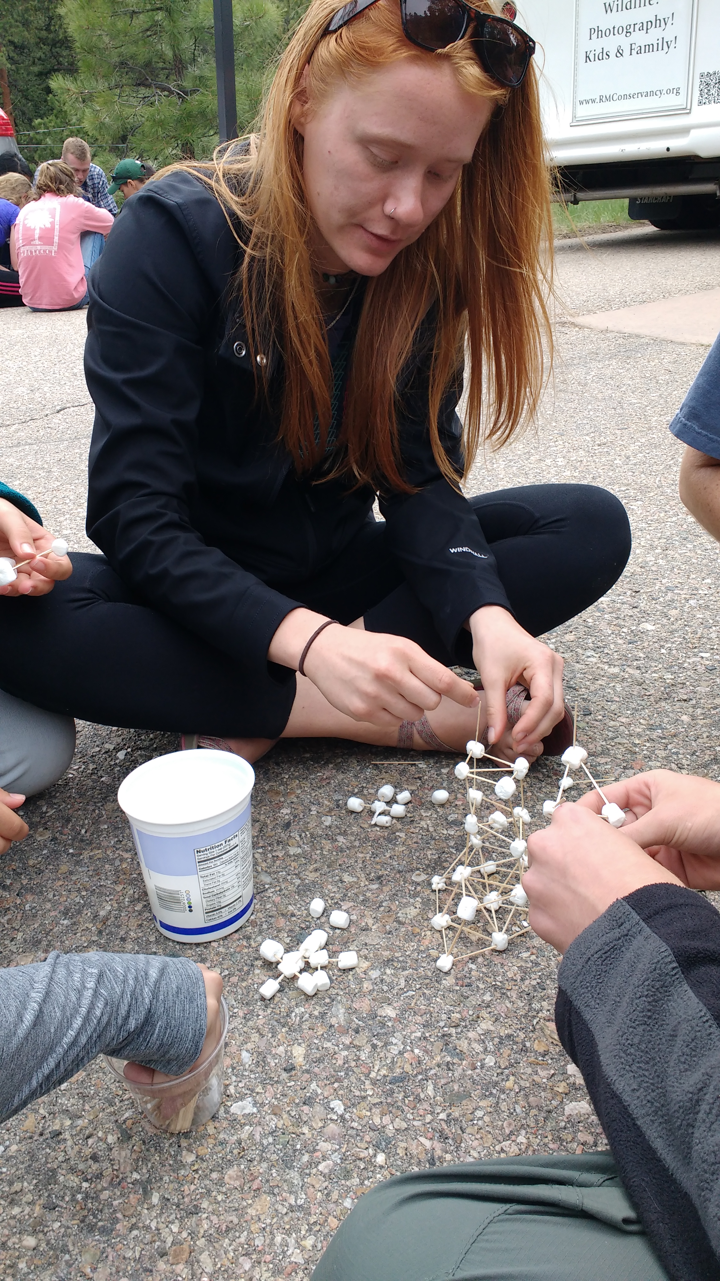 A woman and several others building a geometric structure with sticks and connectors