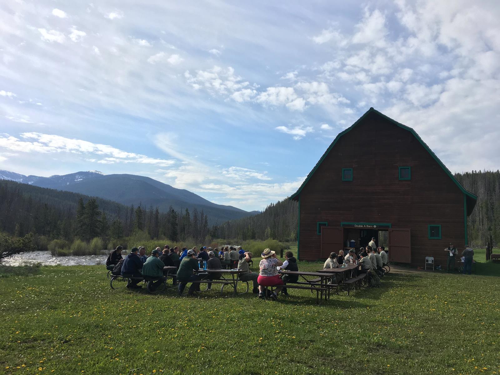 Group of people sitting at picnic tables outside a large red barn