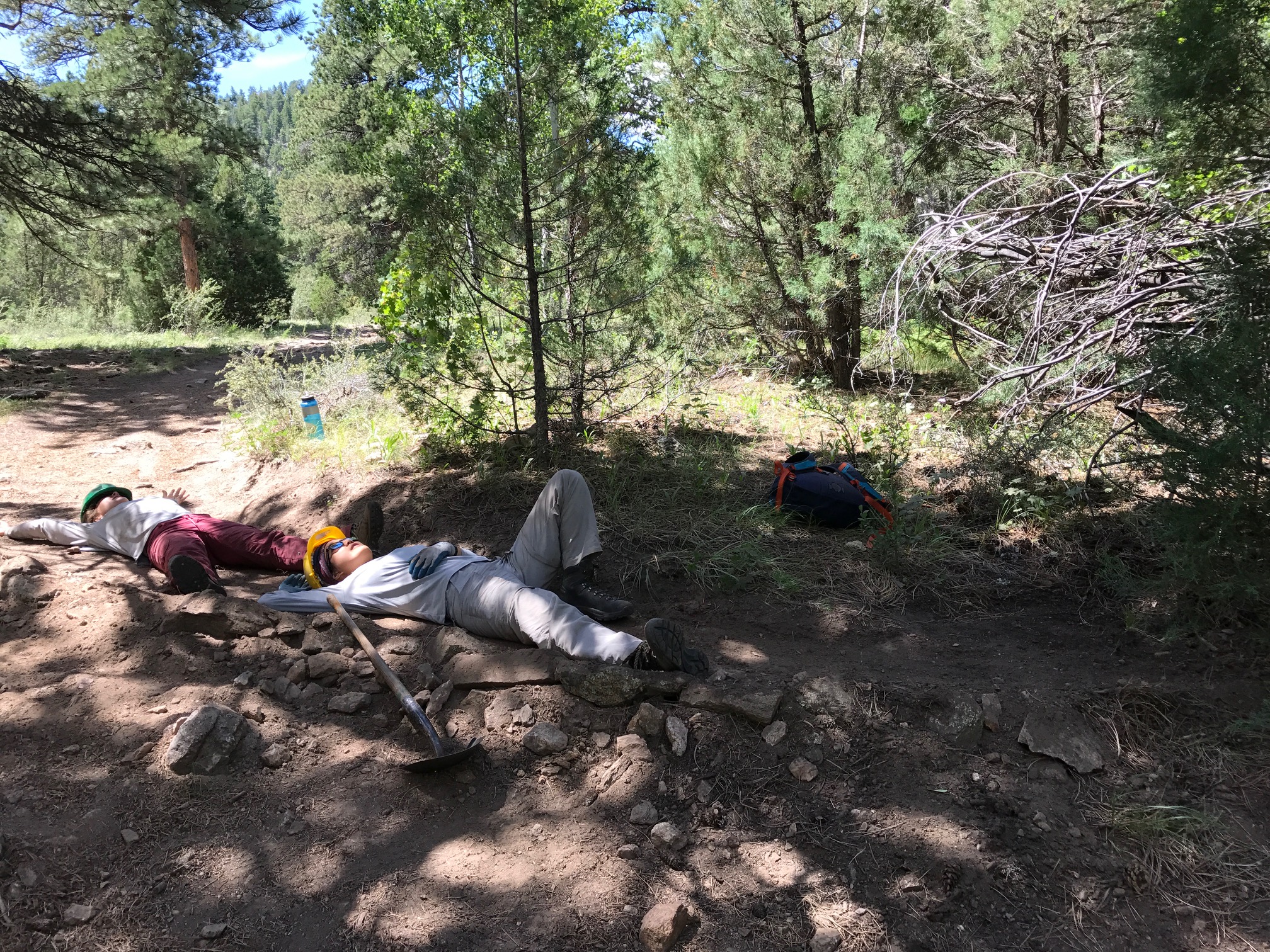 Two people lying on the ground resting next to a hiking trail in a forest