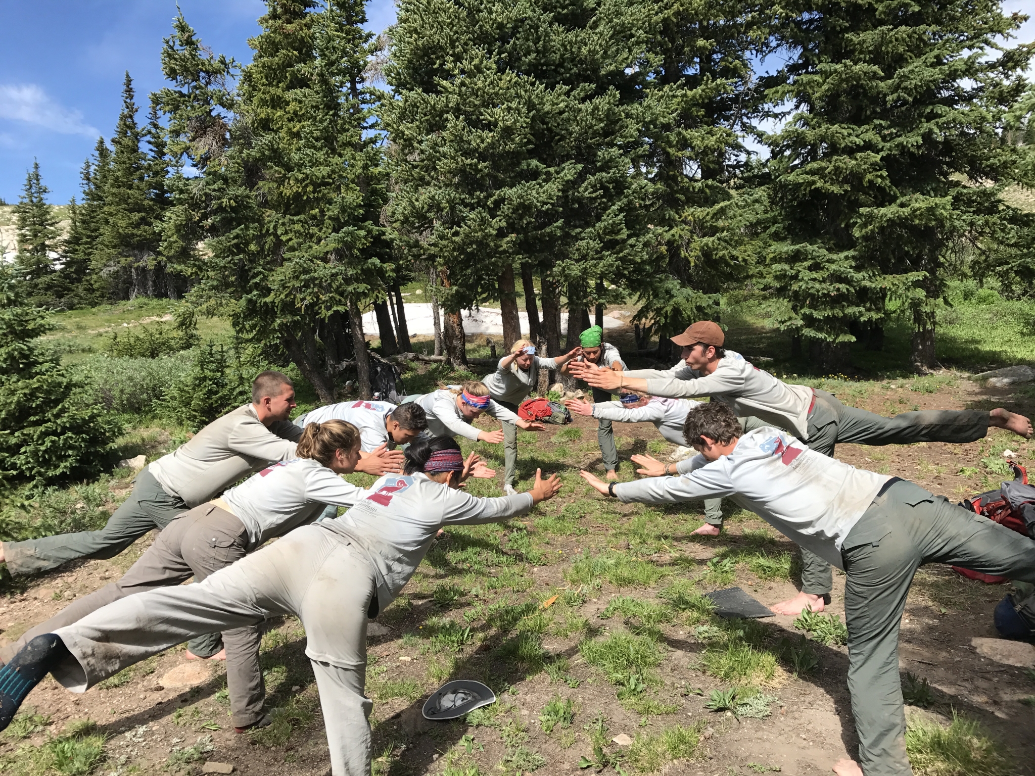 A group of park rangers in uniform playfully mimicking a tug-of-war pose in a forest clearing.