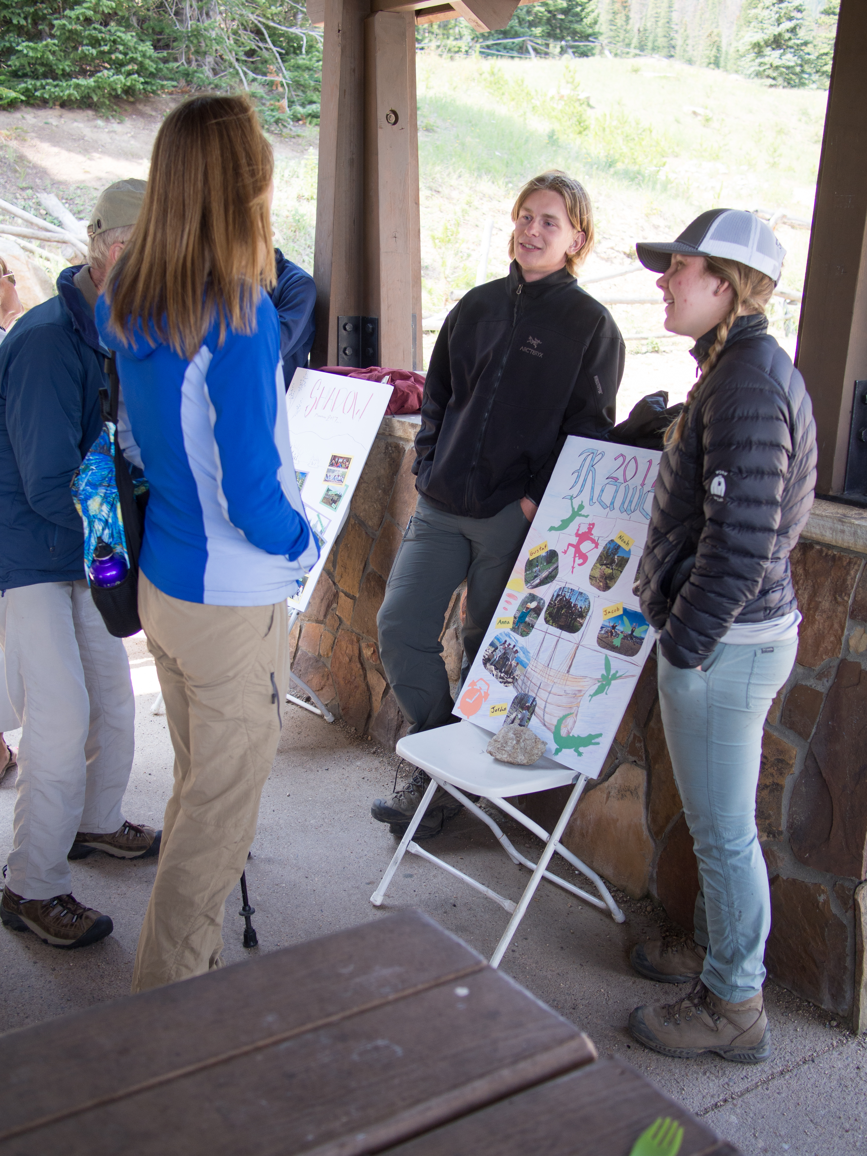 Two people in outdoor clothing standing by an educational poster, interacting with attendees at an environmental event.