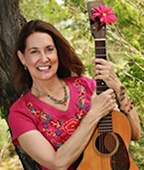 A woman holding an acoustic guitar in front of a tree.