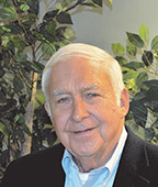 An older man smiling in front of a tree.