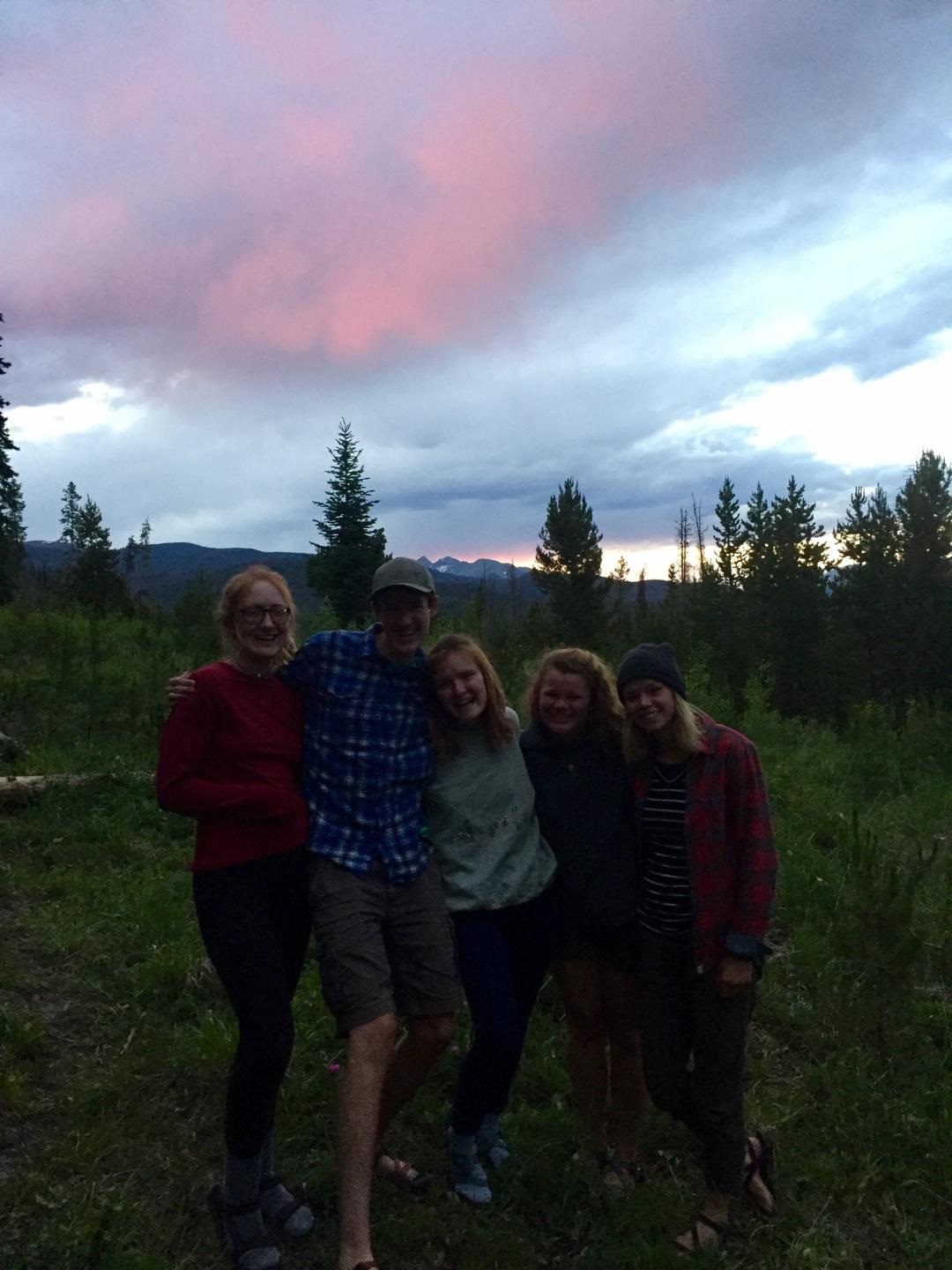 Group of four friends smiling and posing outdoors at dusk