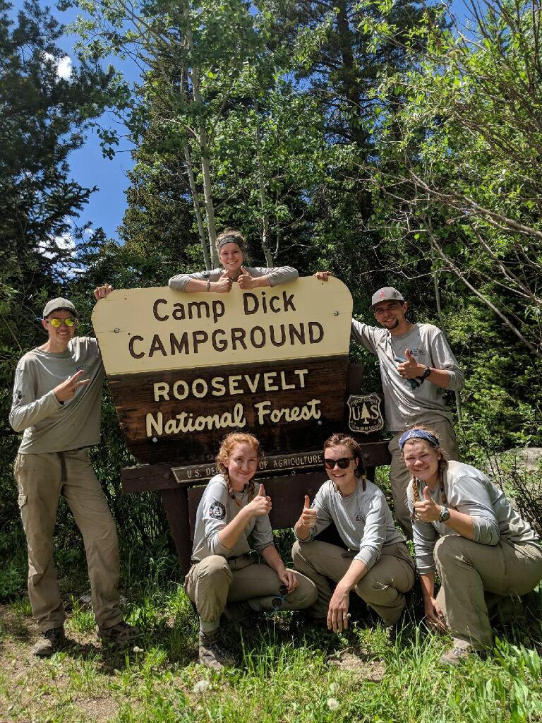 Five people posing with thumbs up around a sign