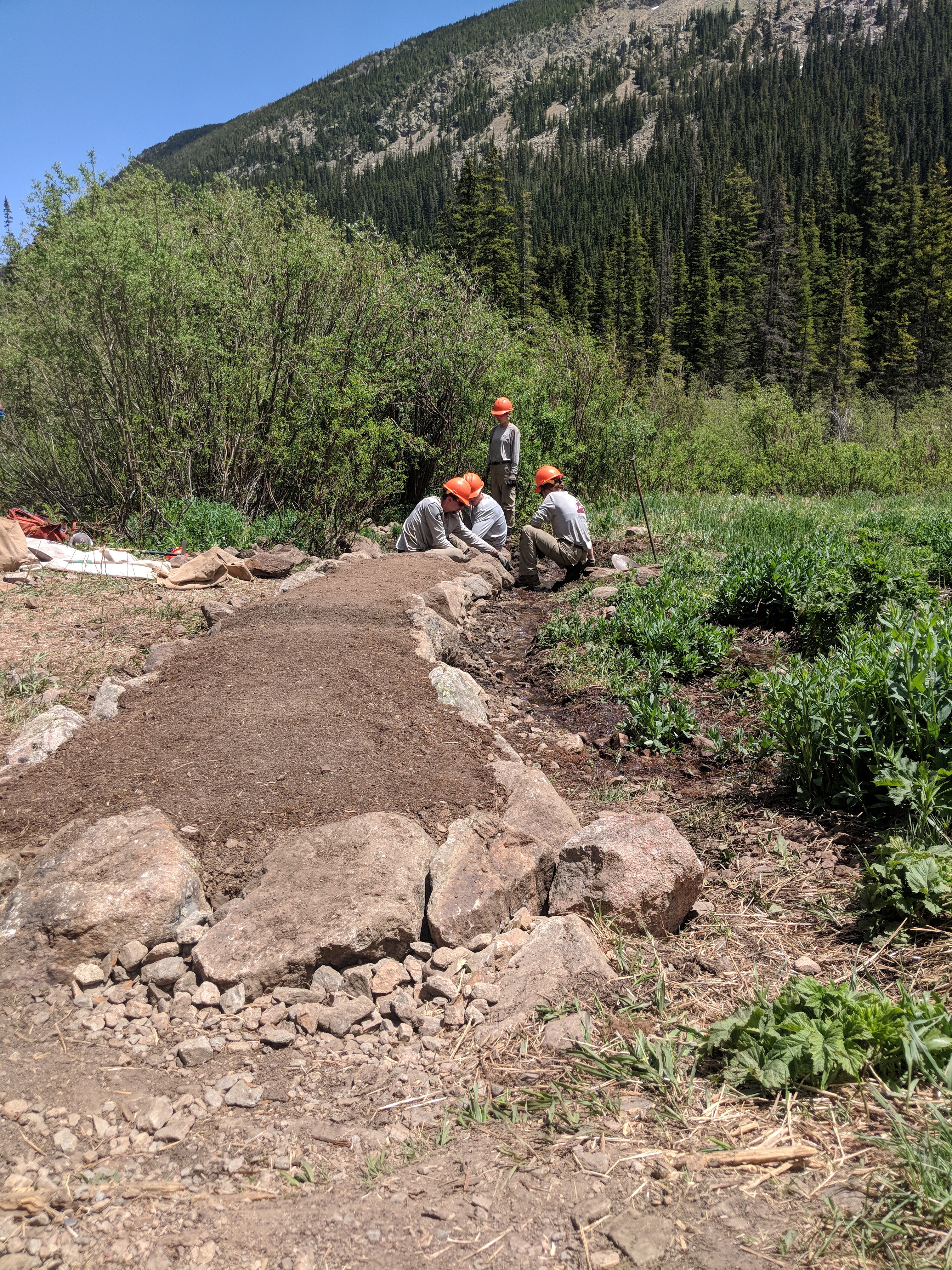 Three workers repair a rocky mountain trail