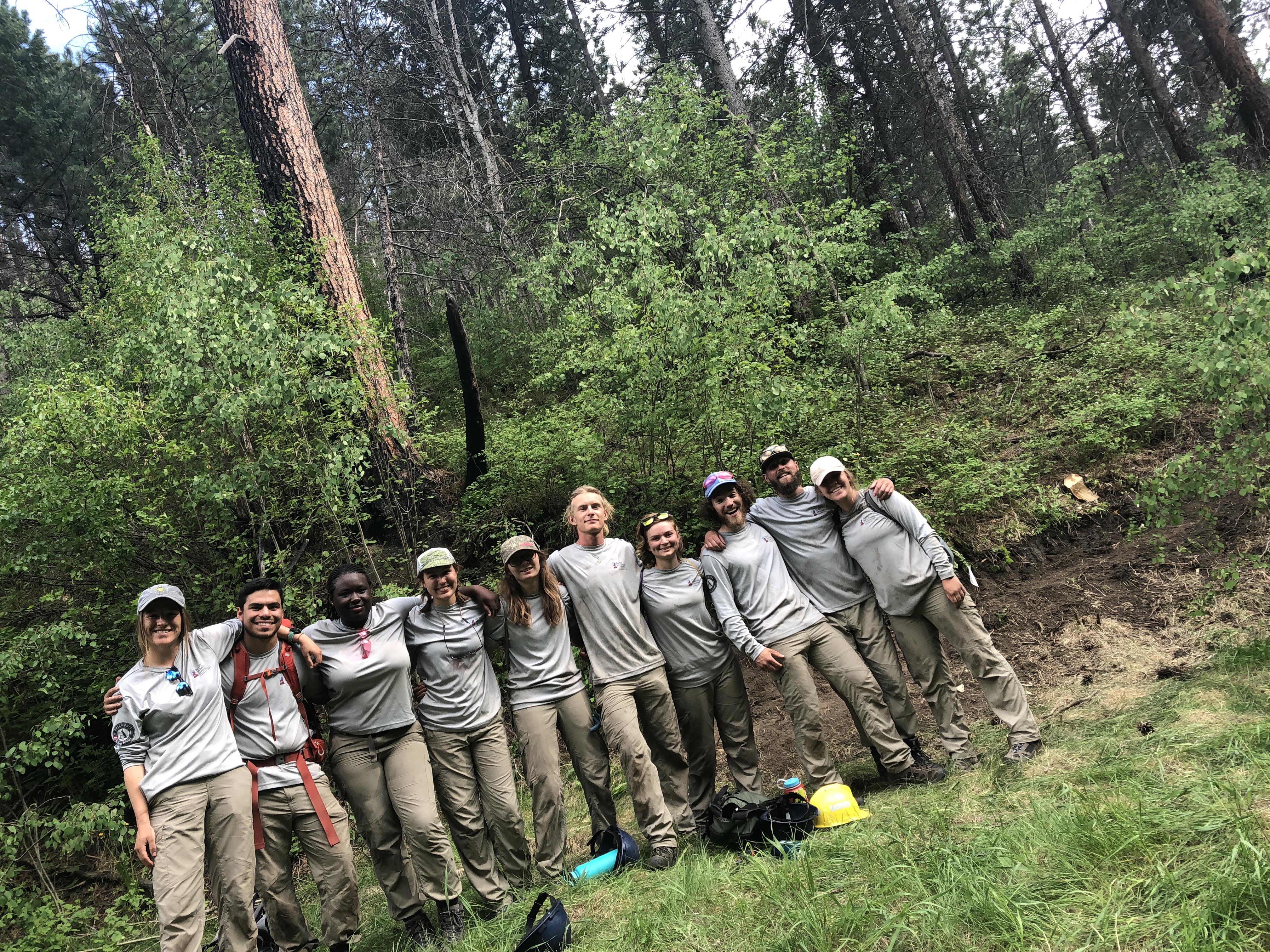 A group of young adults in work uniforms posing together in a lush forest