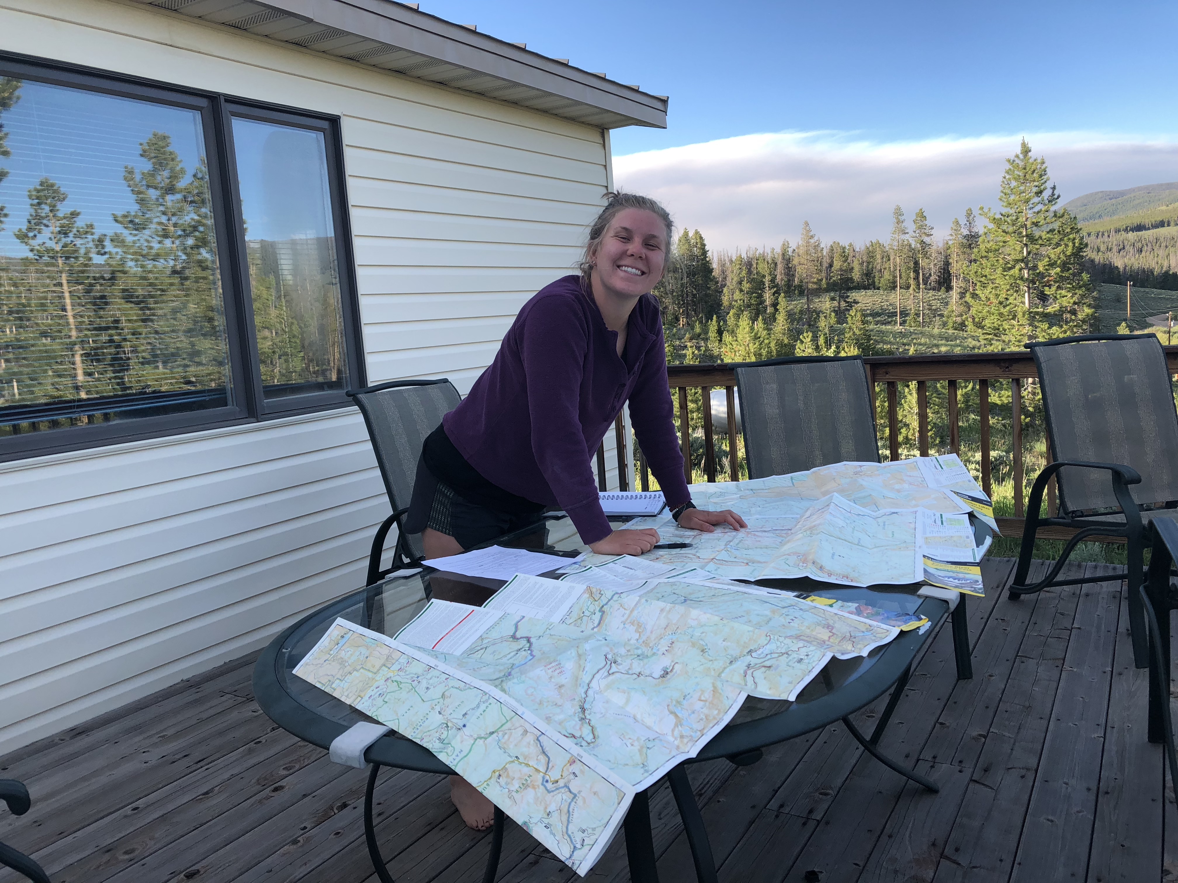 A woman smiles at the camera while examining maps spread out on a table