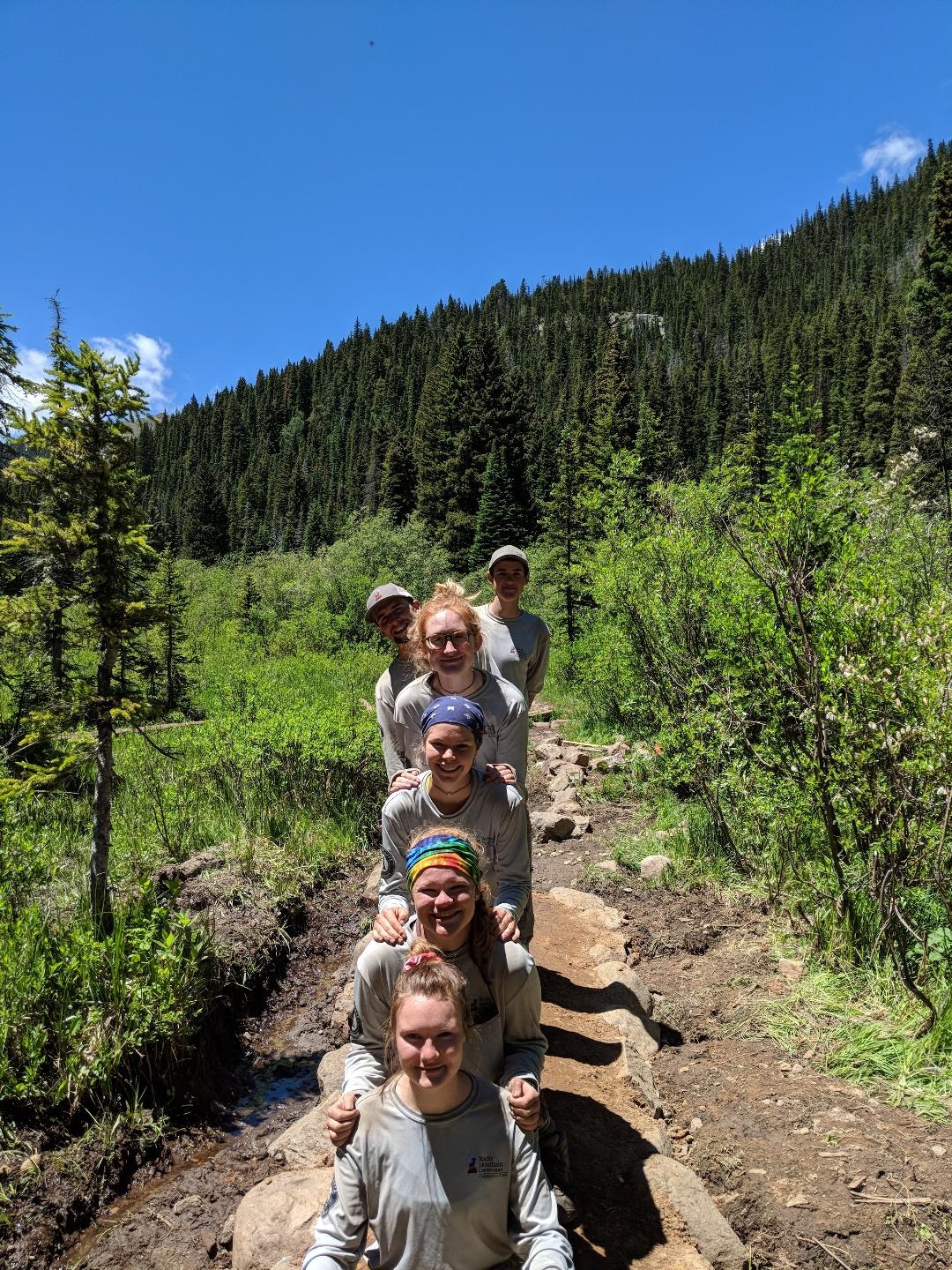 A group of five hikers posing in a line on a forest trail