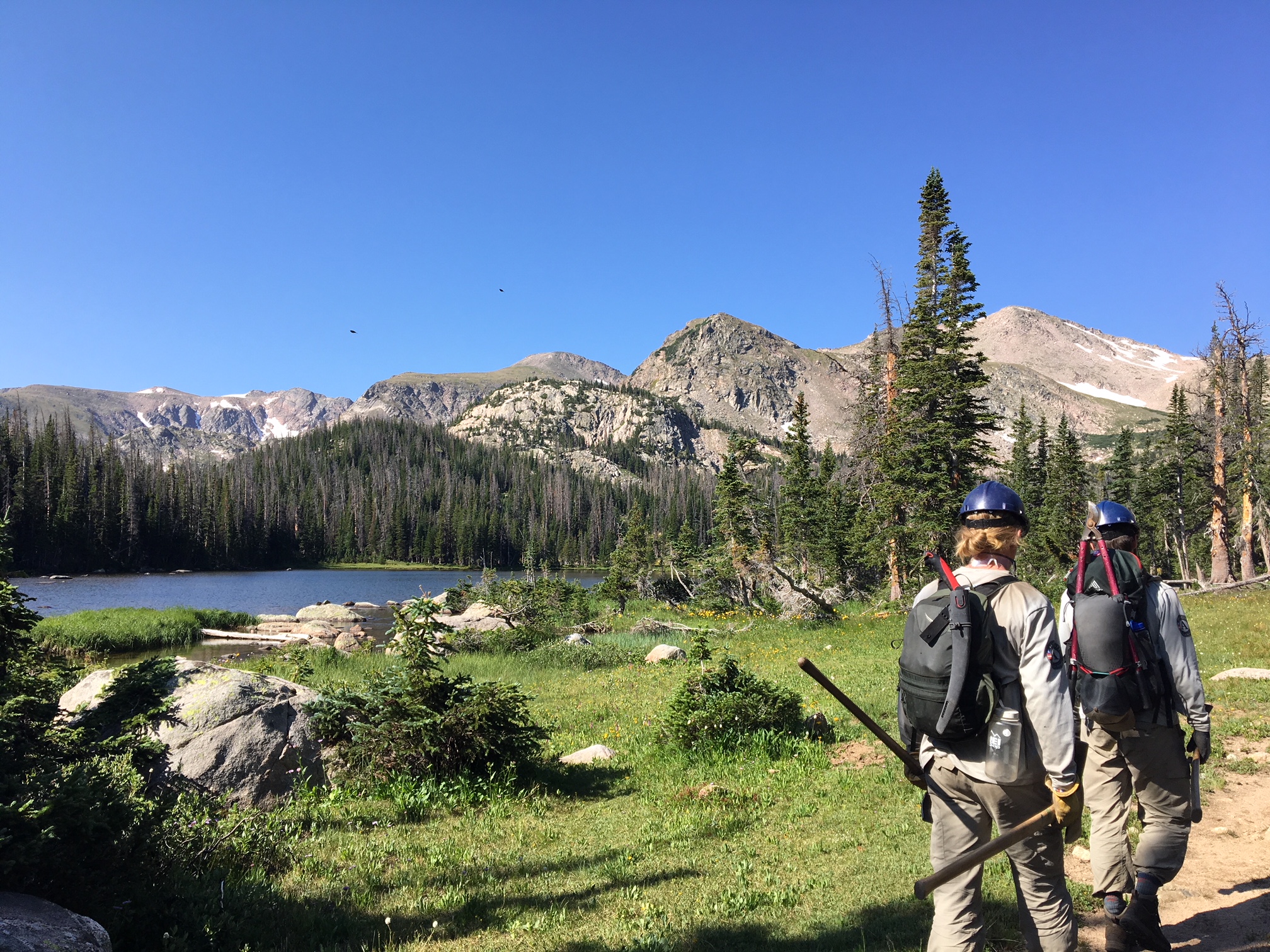 Two hikers walking near a mountain lake