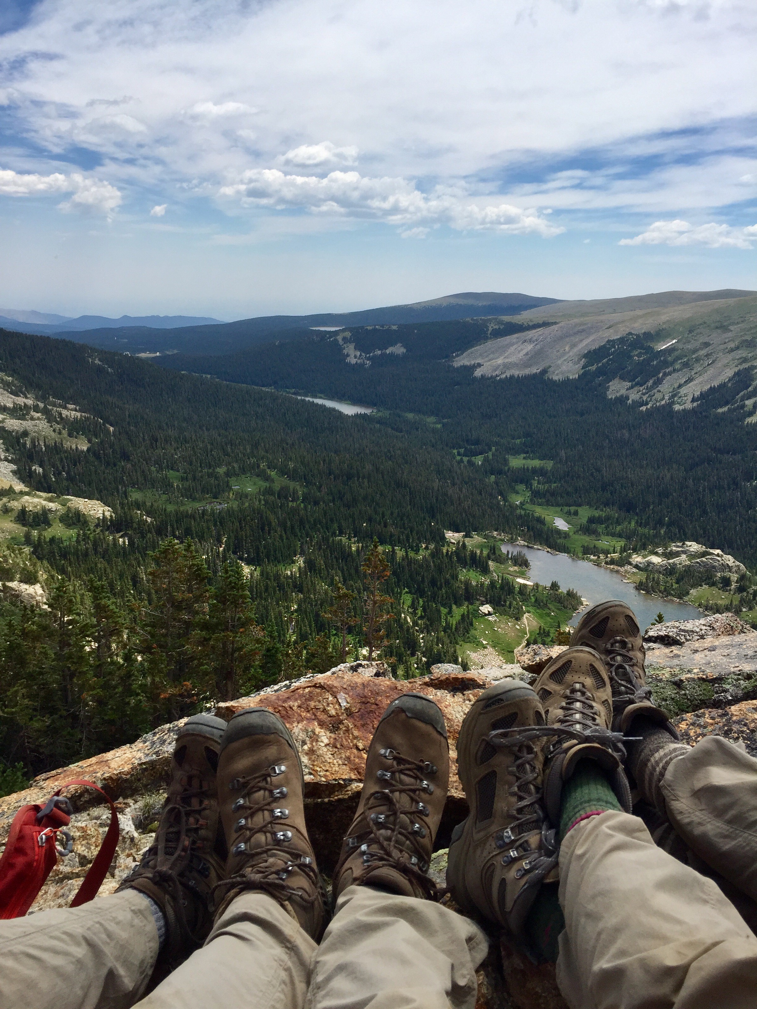 Four people's legs with hiking boots overlooking a scenic valley