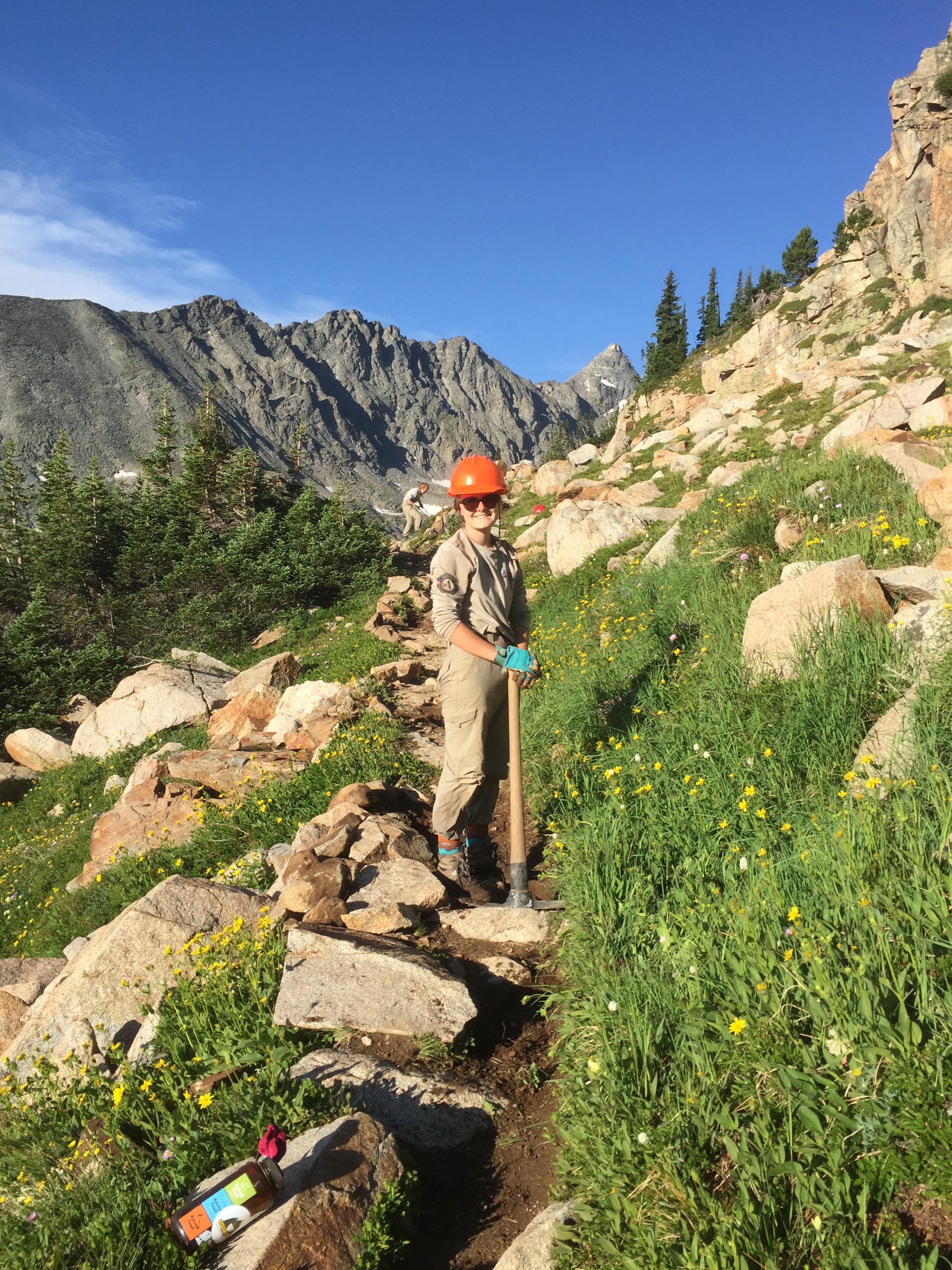 A park ranger standing on a rocky trail in a mountainous area