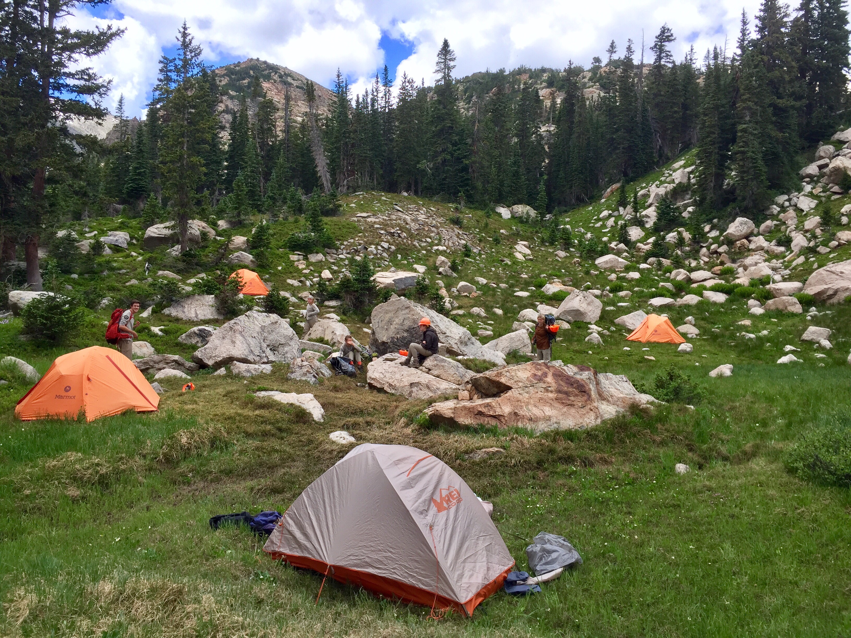 Campers setting up tents among boulders in a forested mountain area 