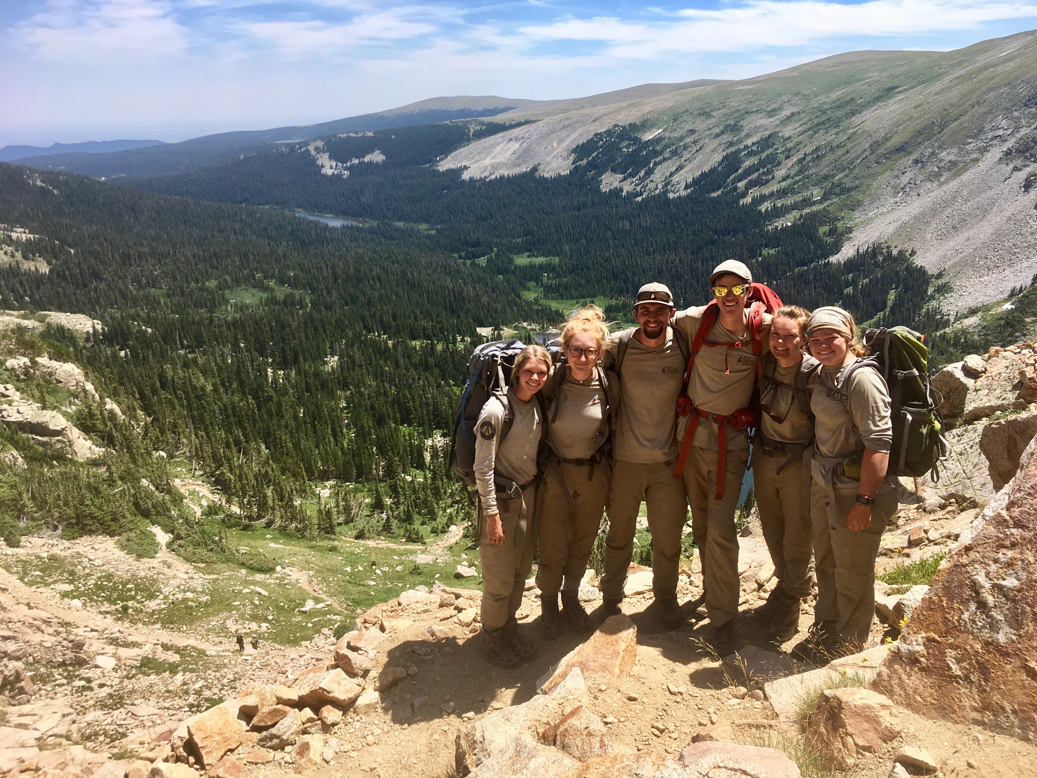 Group of six hikers smiling on a mountain trail