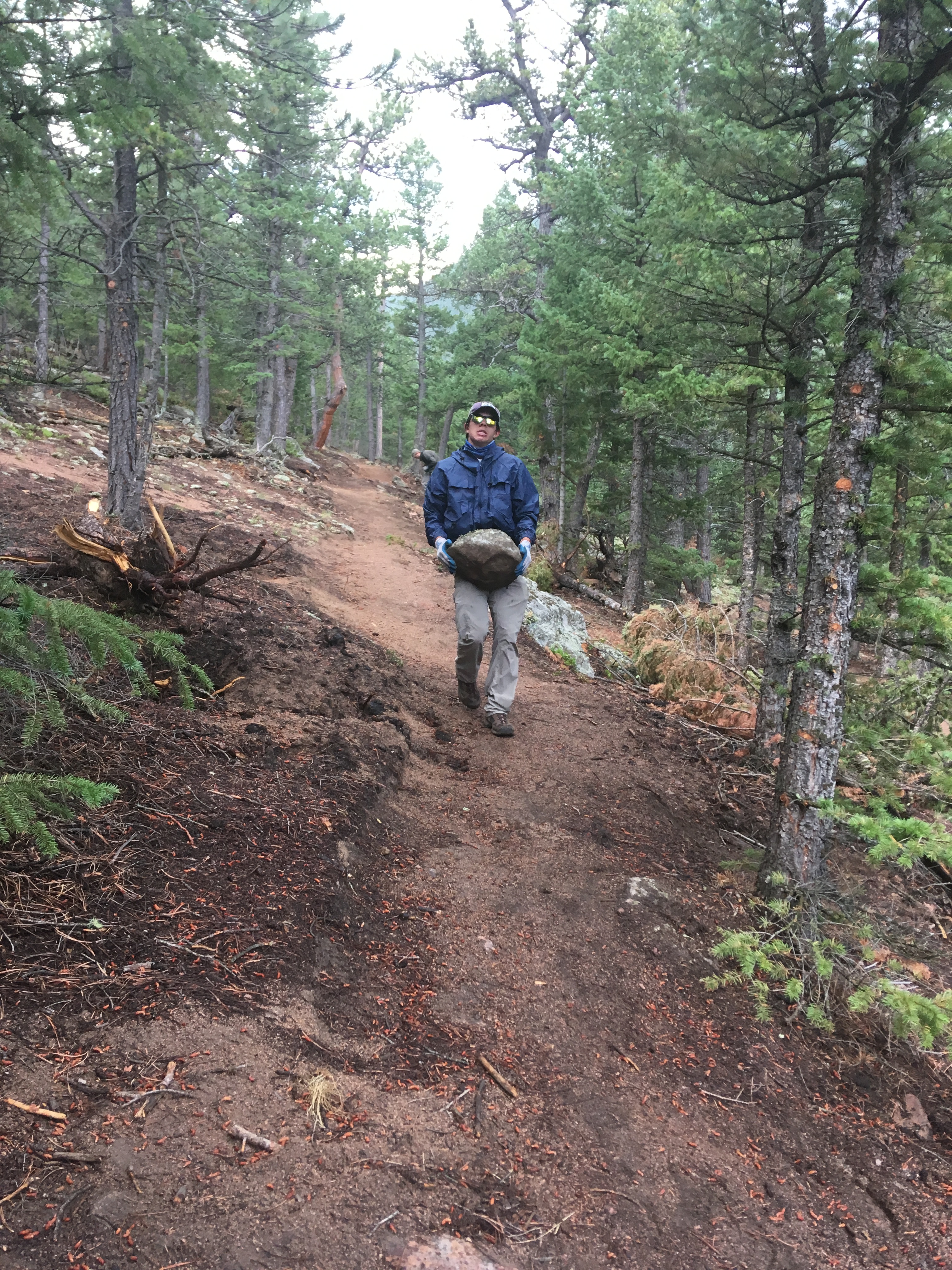 A person carrying a rock across the mountain trail.