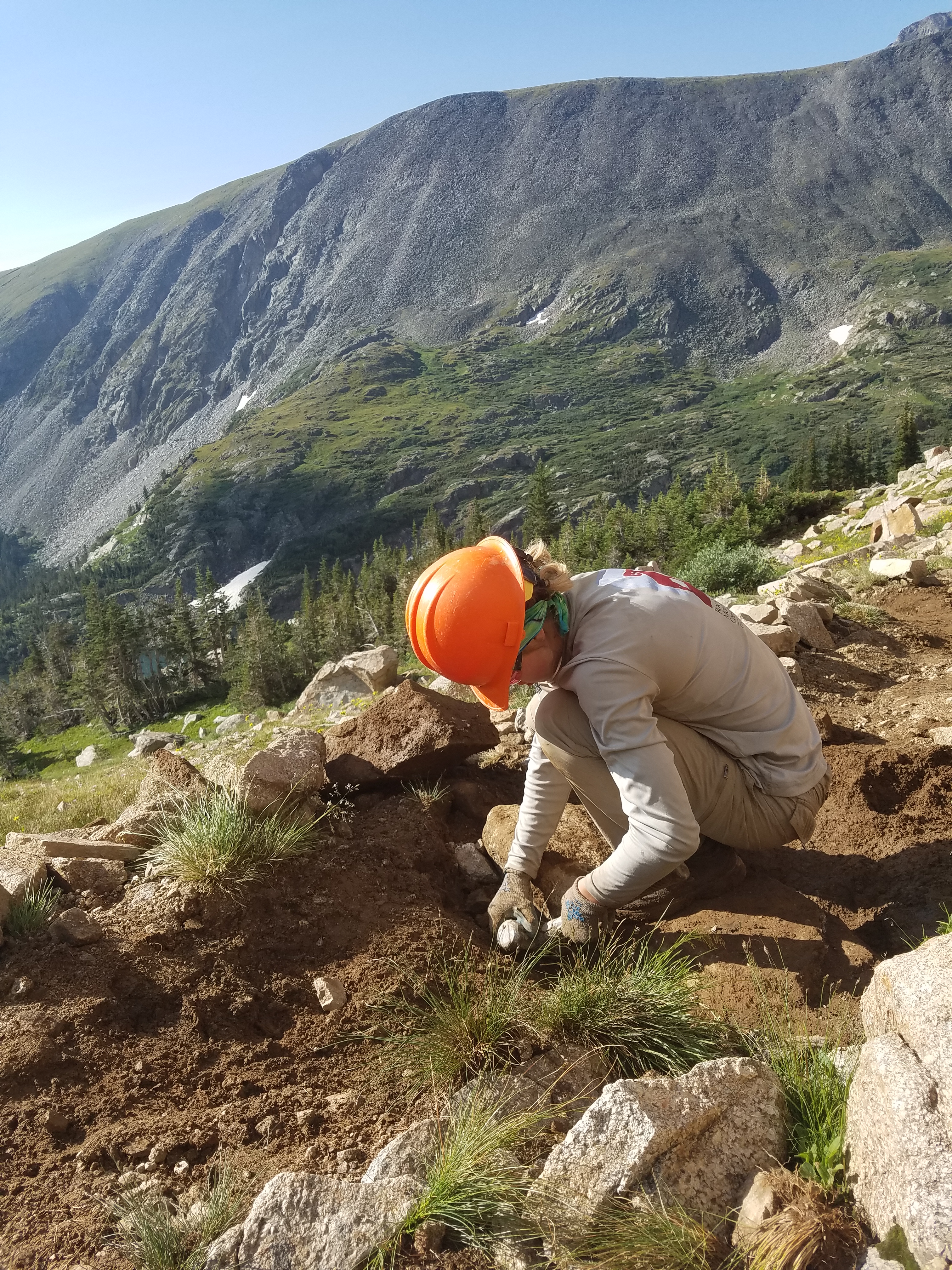 A person wearing safety gear digs in rocky soil