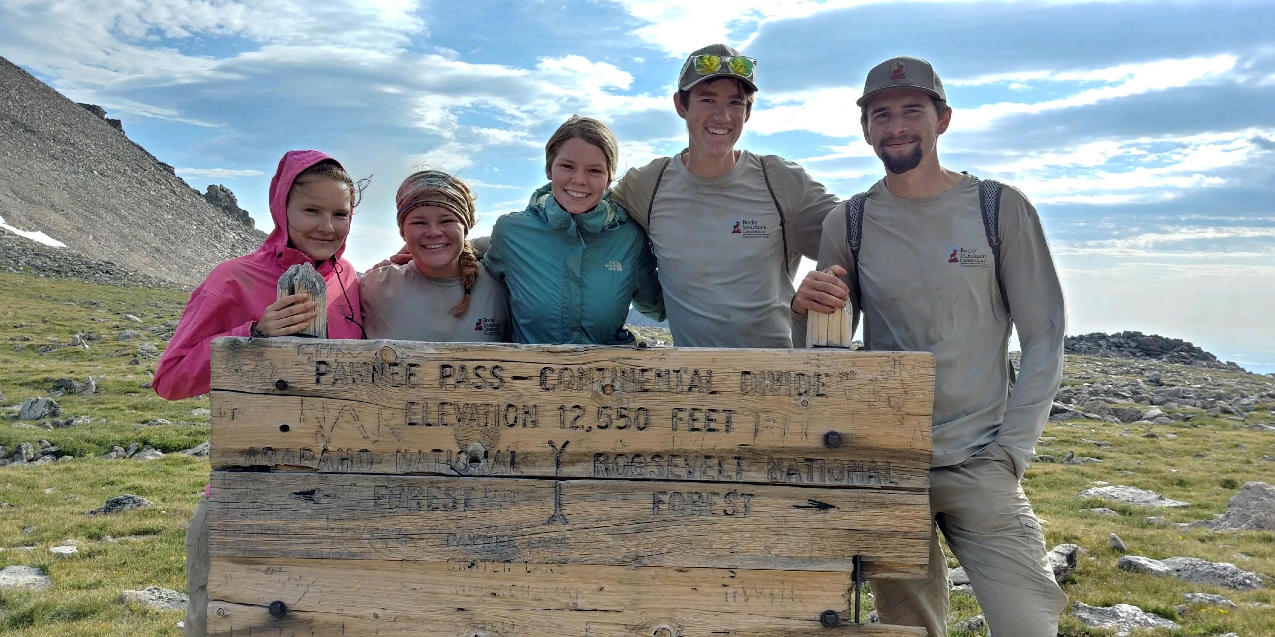 Five person smiling while standing behind a sign