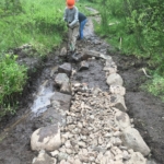 A man is working on a rocky path in the woods.