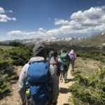 A group of hikers on a trail with mountains in the background.