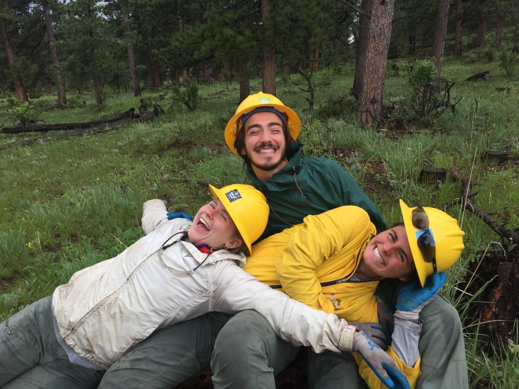 Three people in yellow hats laying on a log.