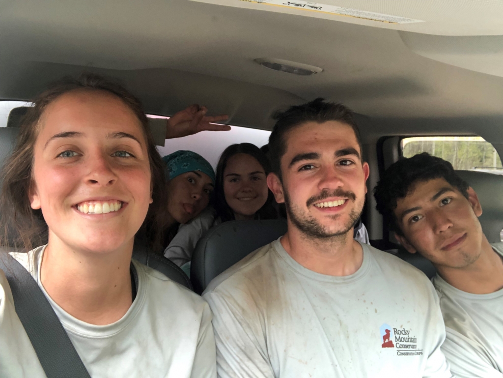 A group of people smiling in the back seat of a car.