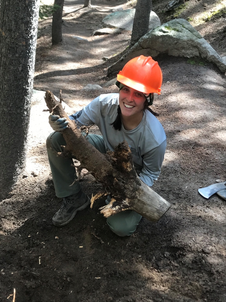 A woman kneeling down in the woods with a log.